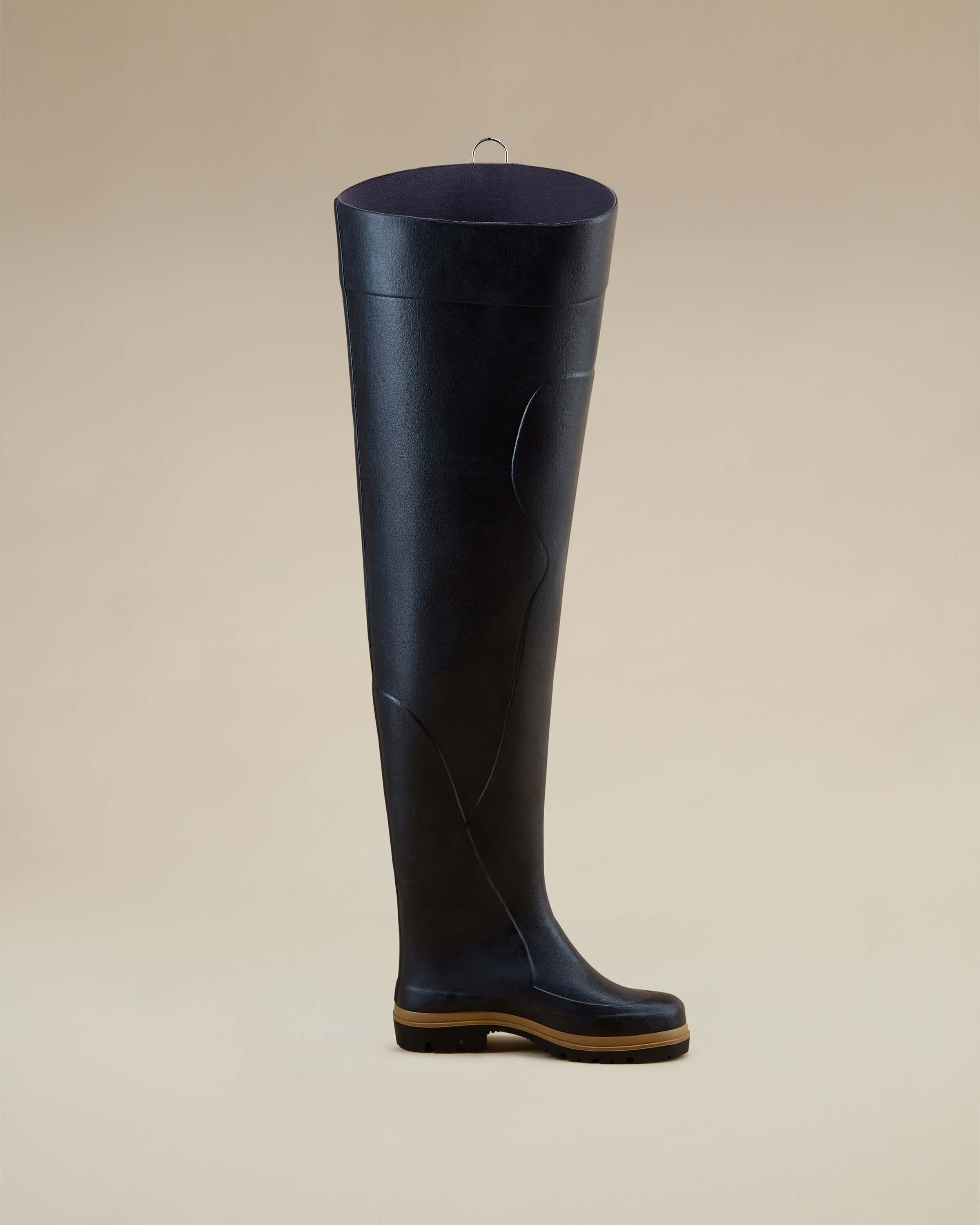 Product photo of a single Men's Océane Ponti Lined Thigh Boot in Black, shown from a profile angle against a neutral beige backdrop. The boot stands upright with a gum-colored sole and no visible fastenings.