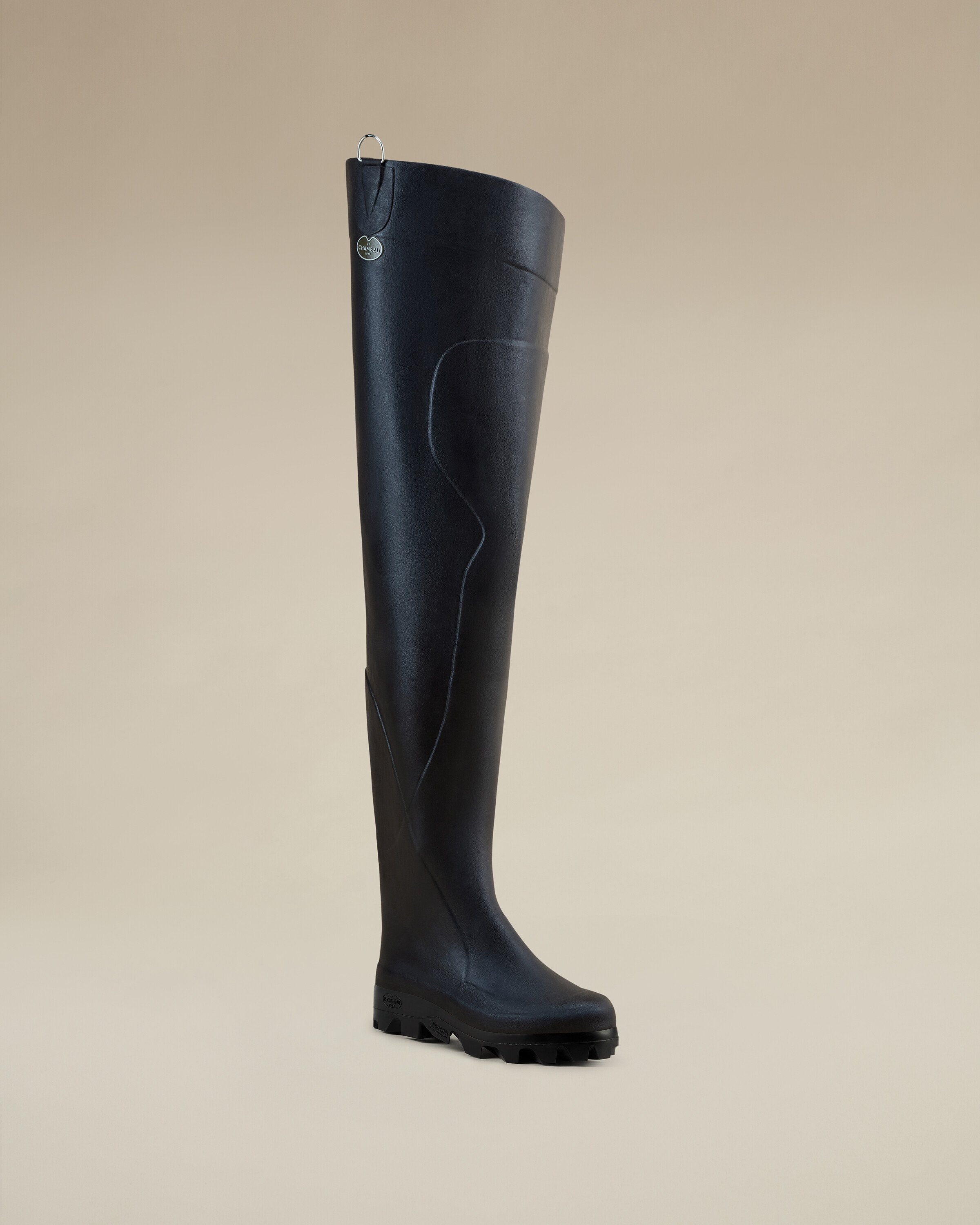 Right profile view of the Men's Océane Ponti Lined Thigh Boot in Black, featuring a gum-colored sole. The boot is set against a beige background and includes a small hanging ring with logo tag.