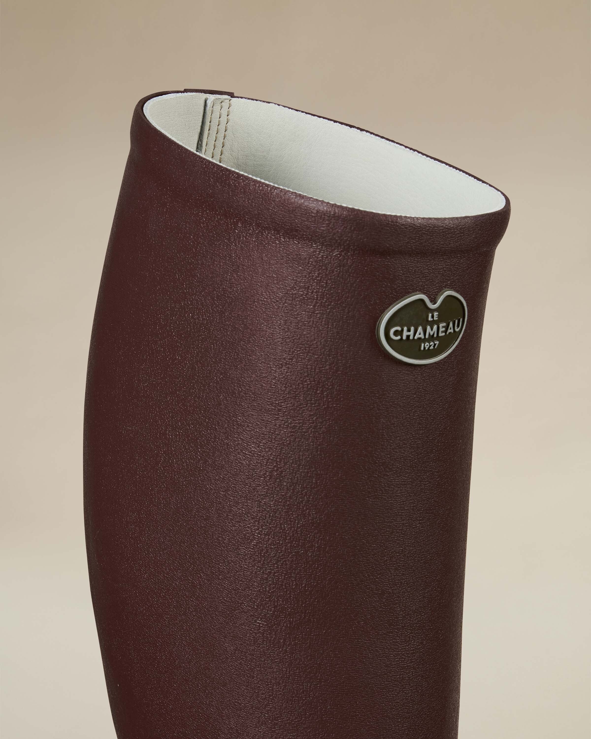 A close-up of the upper section of the Men's Saint Hubert Leather Lined Wellington Boot in Brown highlighting the white leather interior lining, the stitched seam, and the metallic Le Chameau logo badge on the smooth brown exterior.