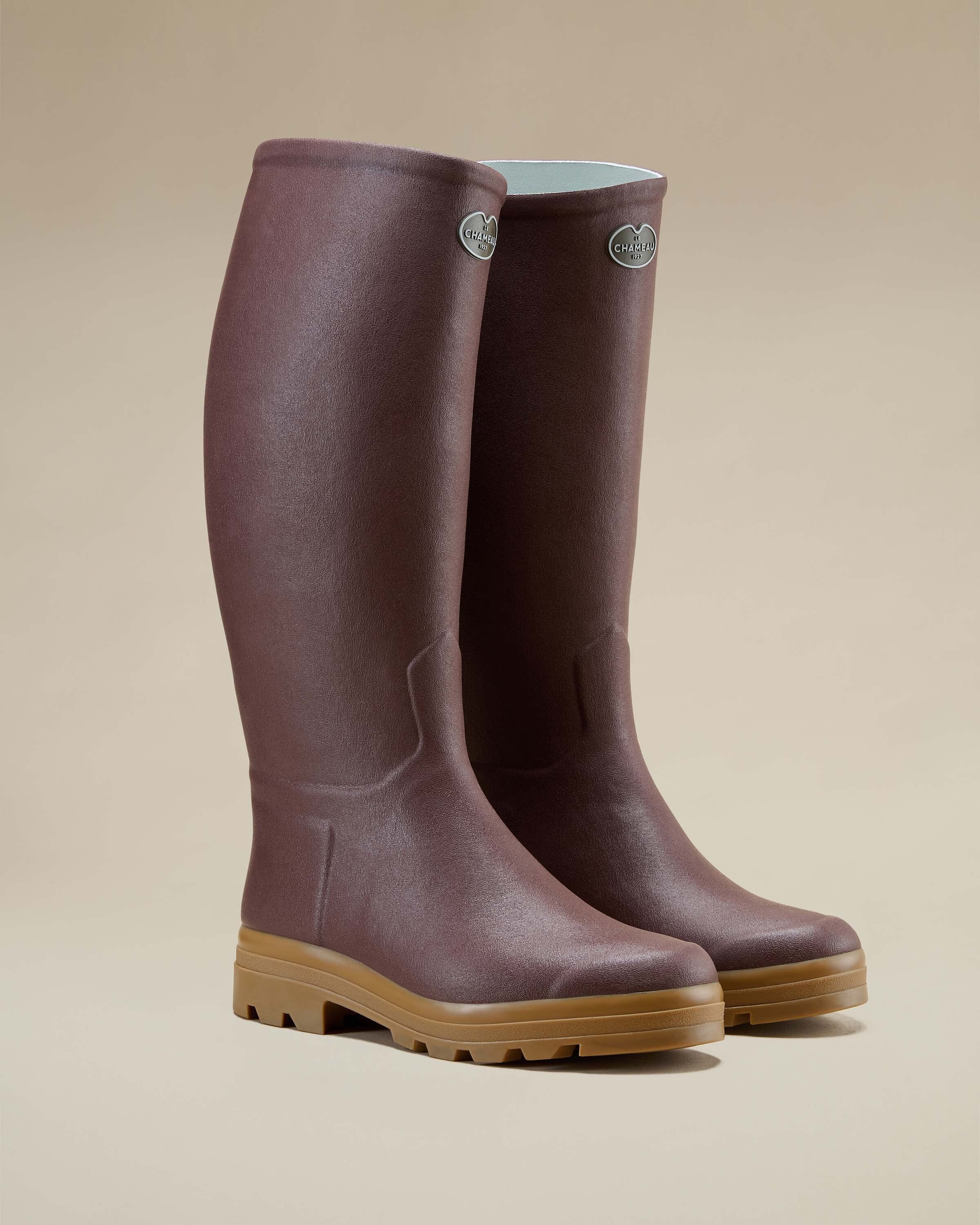 A three-quarter angle of a pair of Men's Saint Hubert Leather Lined Wellington Boot in Brown shown together on a neutral studio backdrop. The boots stand upright, showcasing their tall shaft and light interior lining with the brand logo badge near the top.