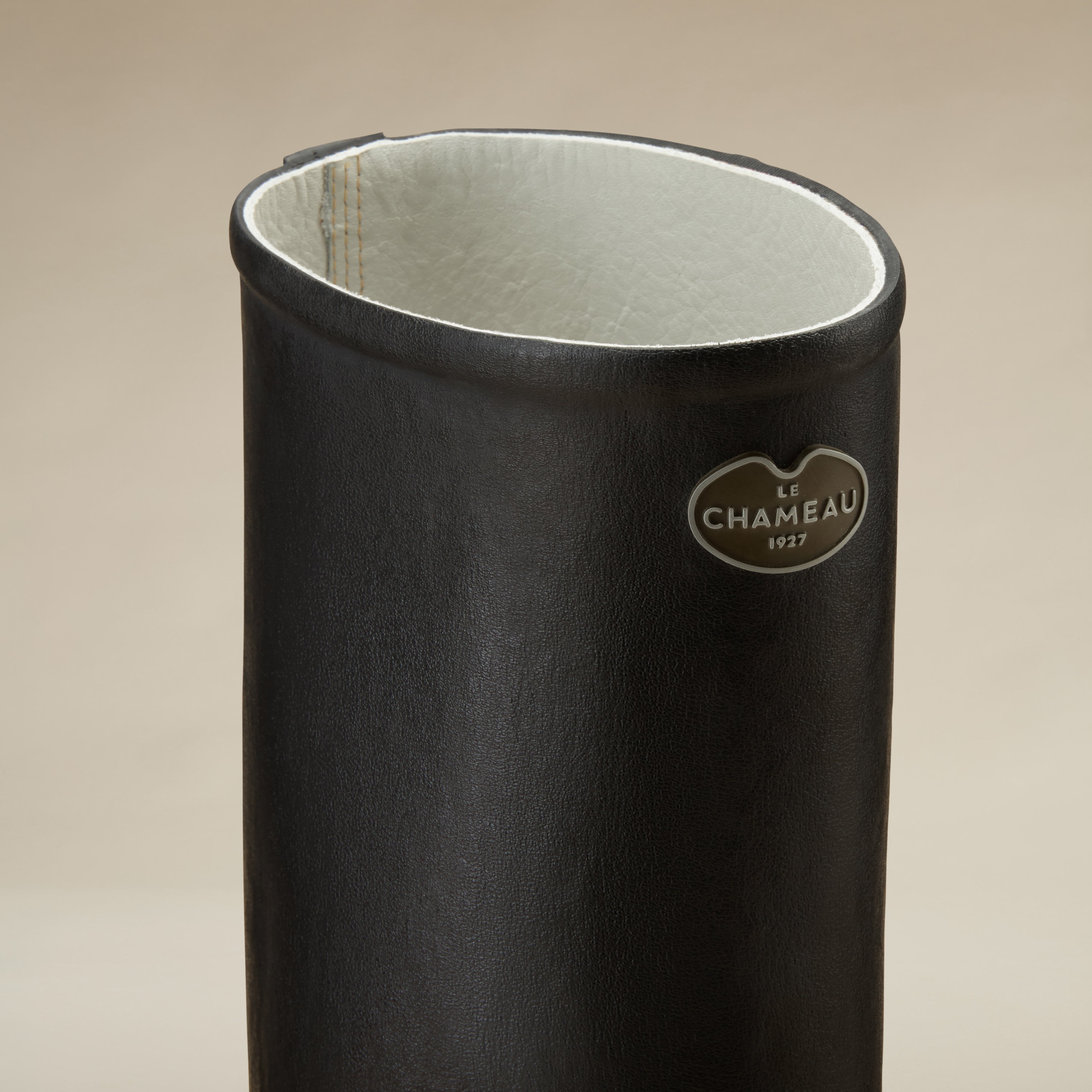 A close-up image of the top of the Men's Saint Hubert Leather Lined Wellington Boot in Black shaft showing the inside leather lining in light cream and the Le Chameau logo badge affixed on the outer shaft near the rim.
