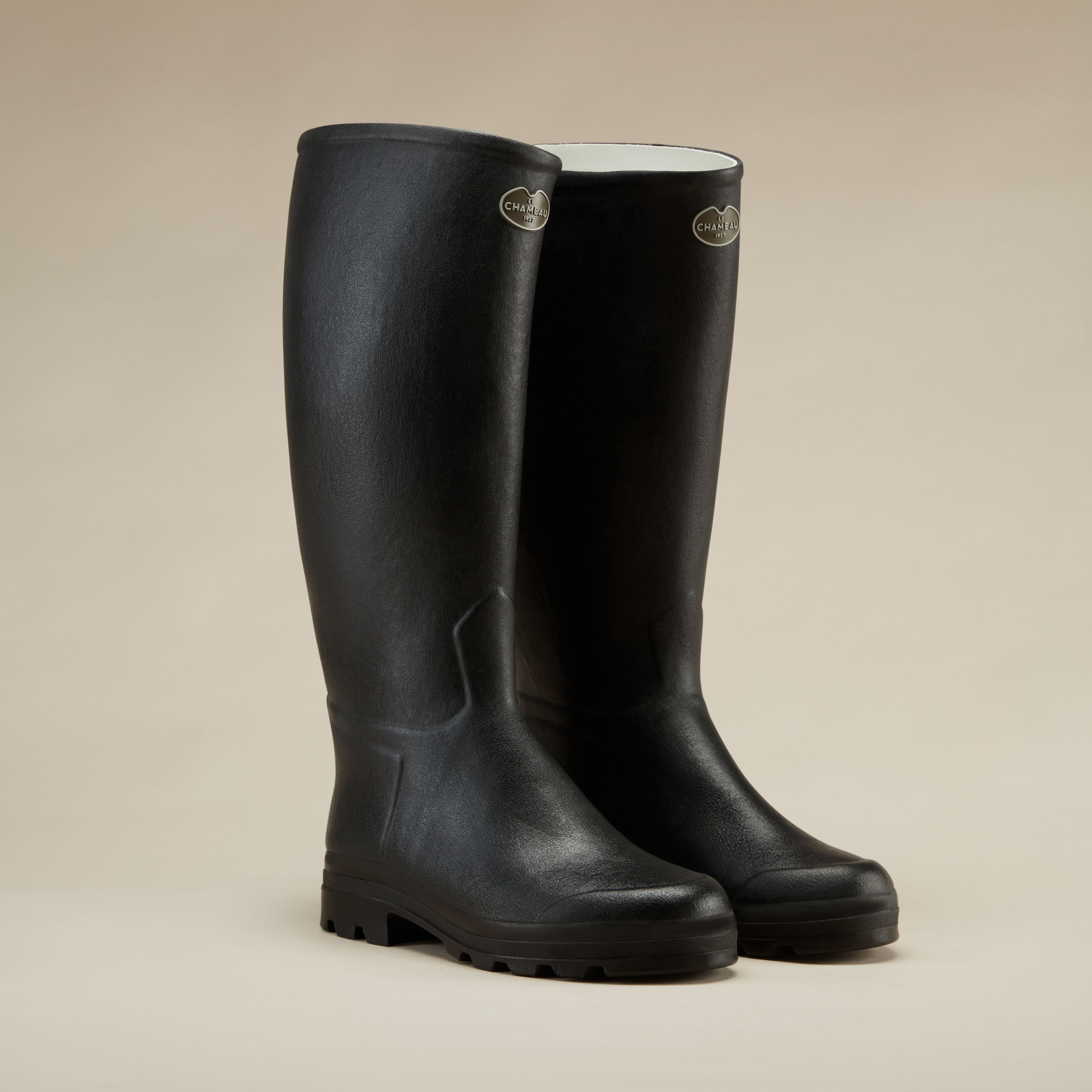 A pair of the Men's Saint Hubert Leather Lined Wellington Boot in Black standing upright on a beige background. The boots are shown from a three-quarter front angle, showcasing their tall shaft height and contoured shaping.