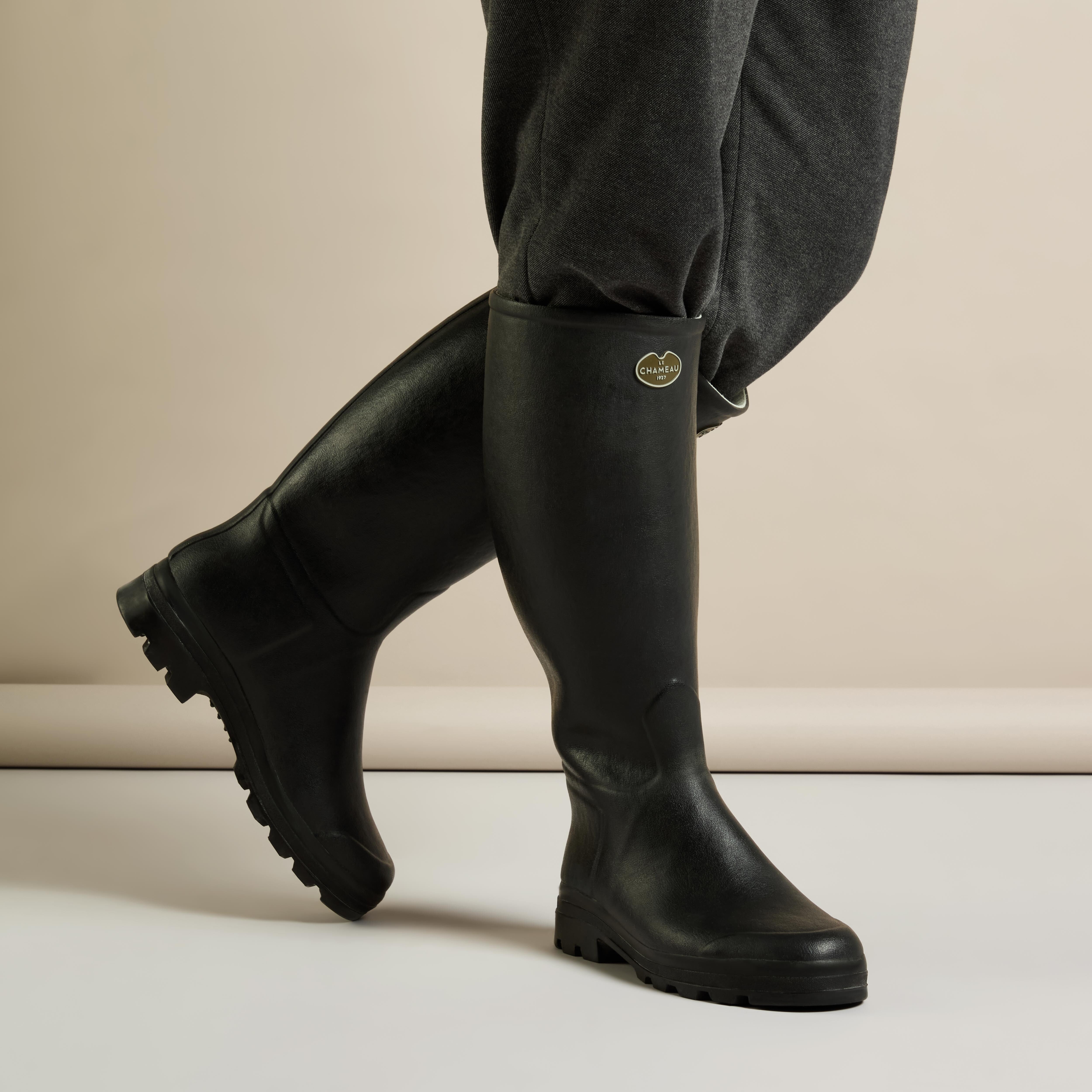 A second lifestyle shot showing a person crossing one leg over the other while wearing the Men's Saint Hubert Leather Lined Wellington Boot in Black. This angle highlights the flexibility and form-fitting design of the boot in motion.