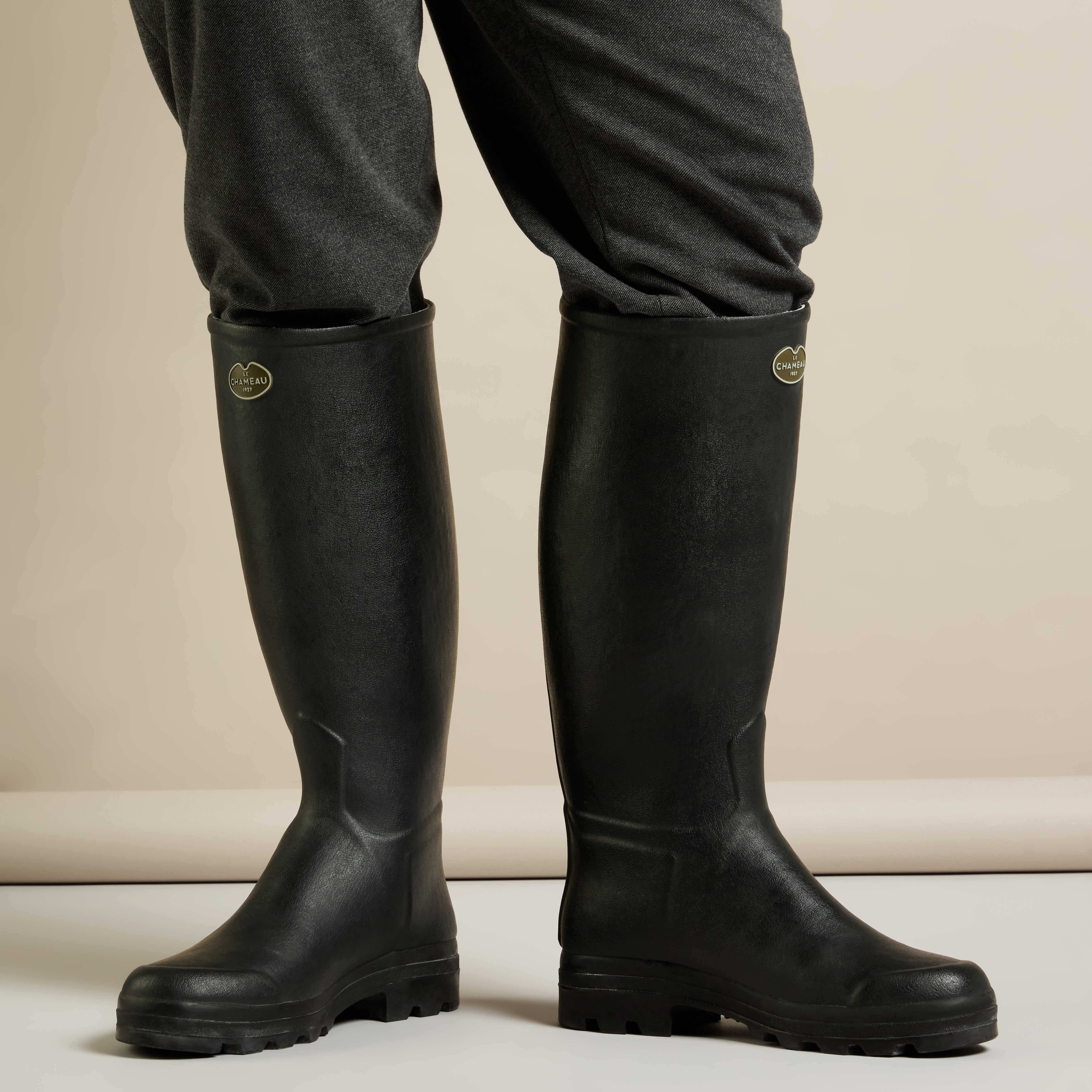 A lifestyle shot showing a person wearing the Men's Saint Hubert Leather Lined Wellington Boot in Black over dark trousers. The image captures a frontal view with the boots standing firmly side by side, emphasizing their height and fit.