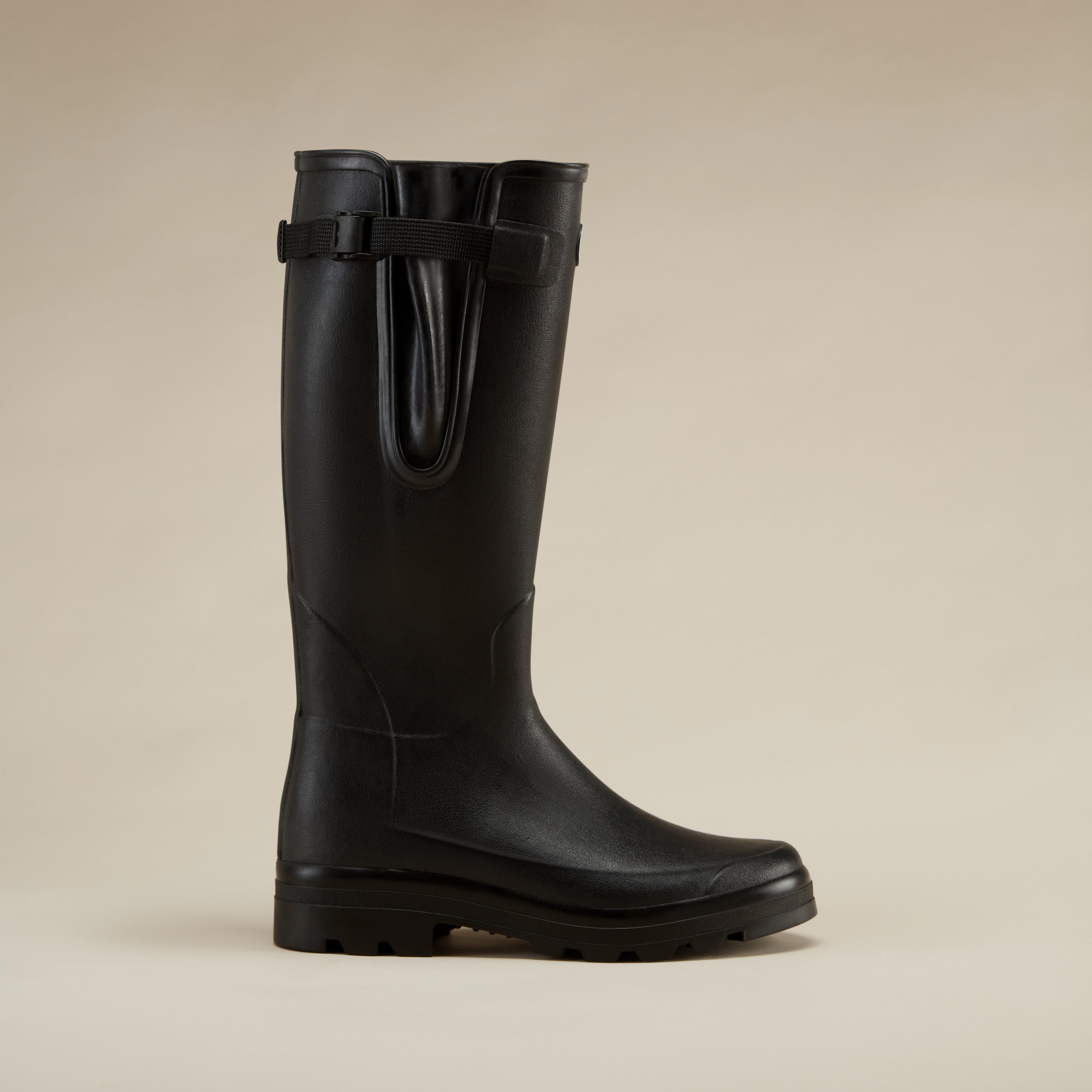 Straight side profile image of the Men's Vierzonord Neoprene Lined Wellington Boot in Black, similar to image 1 but set against a soft beige background for a warmer visual tone. The boot stands independently with a clear view of the tread and upper design lines.
