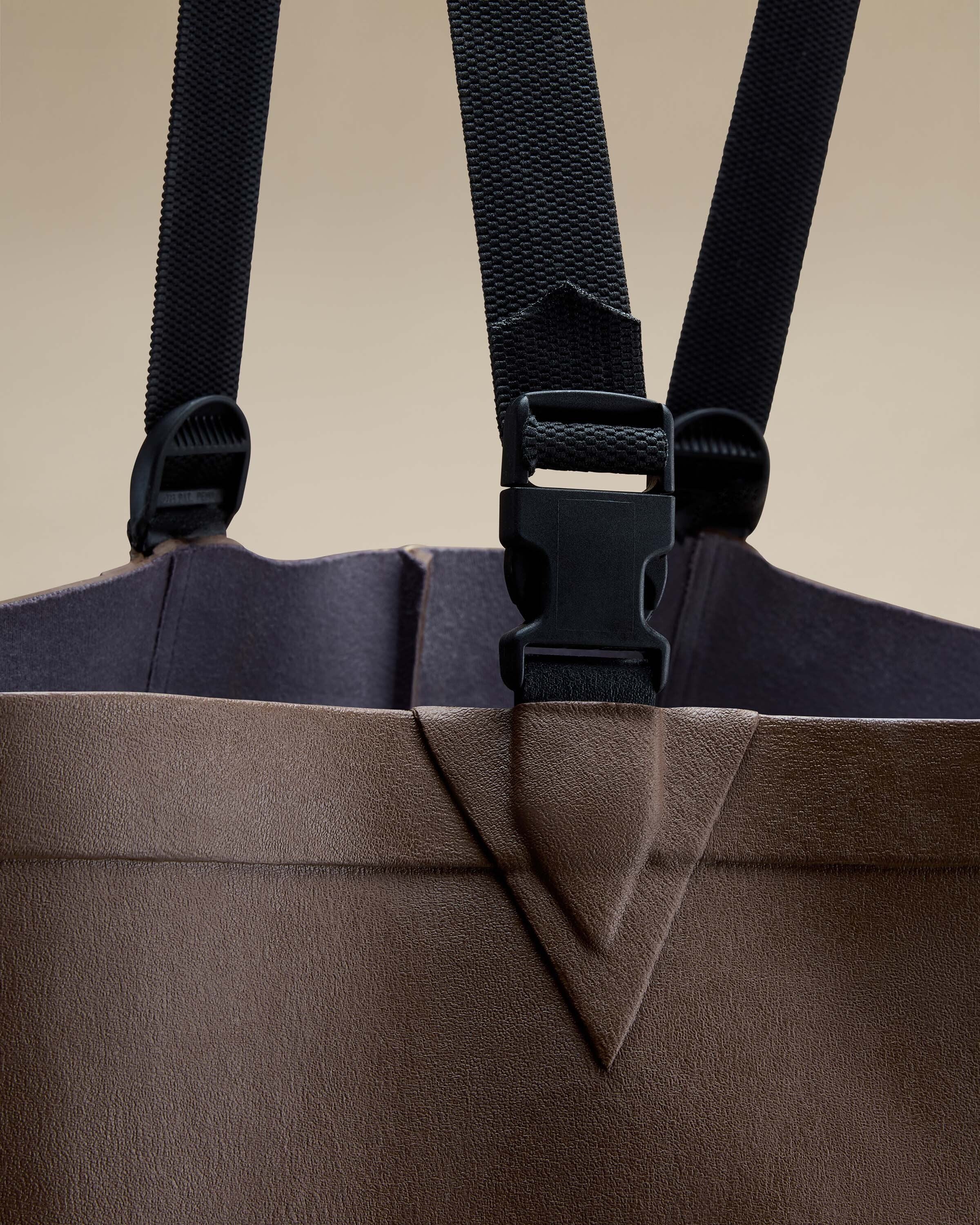 A zoomed-in image focusing on one of the black adjustable straps and its attachment to the Mer Renforcé Waders in Brown. The image emphasises the stitching, clasp mechanism, and rugged rubber texture.