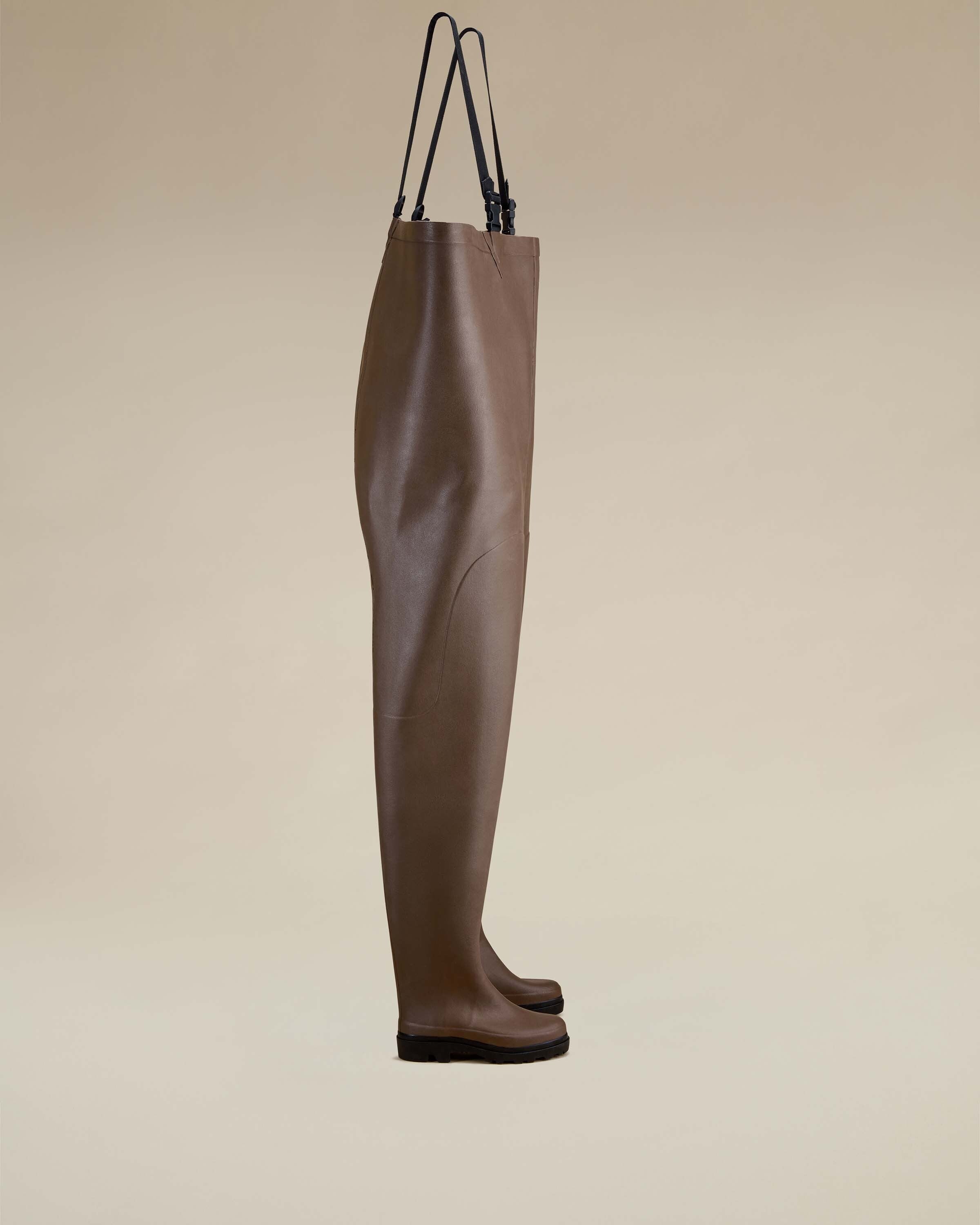 The same side profile of the Mer Renforcé Waders in Brown, now displayed against a soft beige background to emphasize texture and detail. The straps are extended, and the material’s slight sheen is visible.