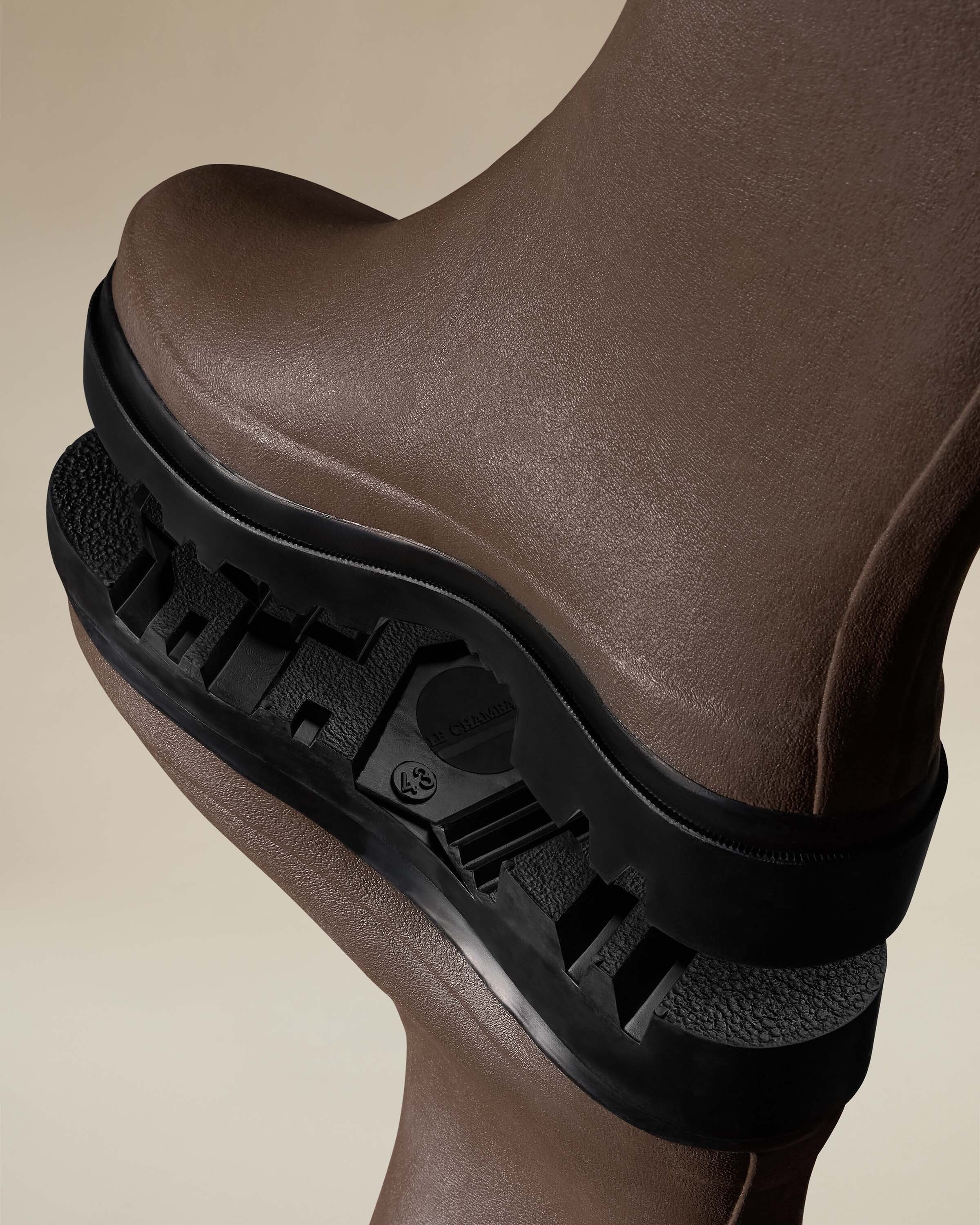 A dynamic angled shot of the Mer Renforcé Waders in Brown's black rubber soles stacked, showcasing the deep tread pattern designed for traction and durability, with size and branding molded into the base.