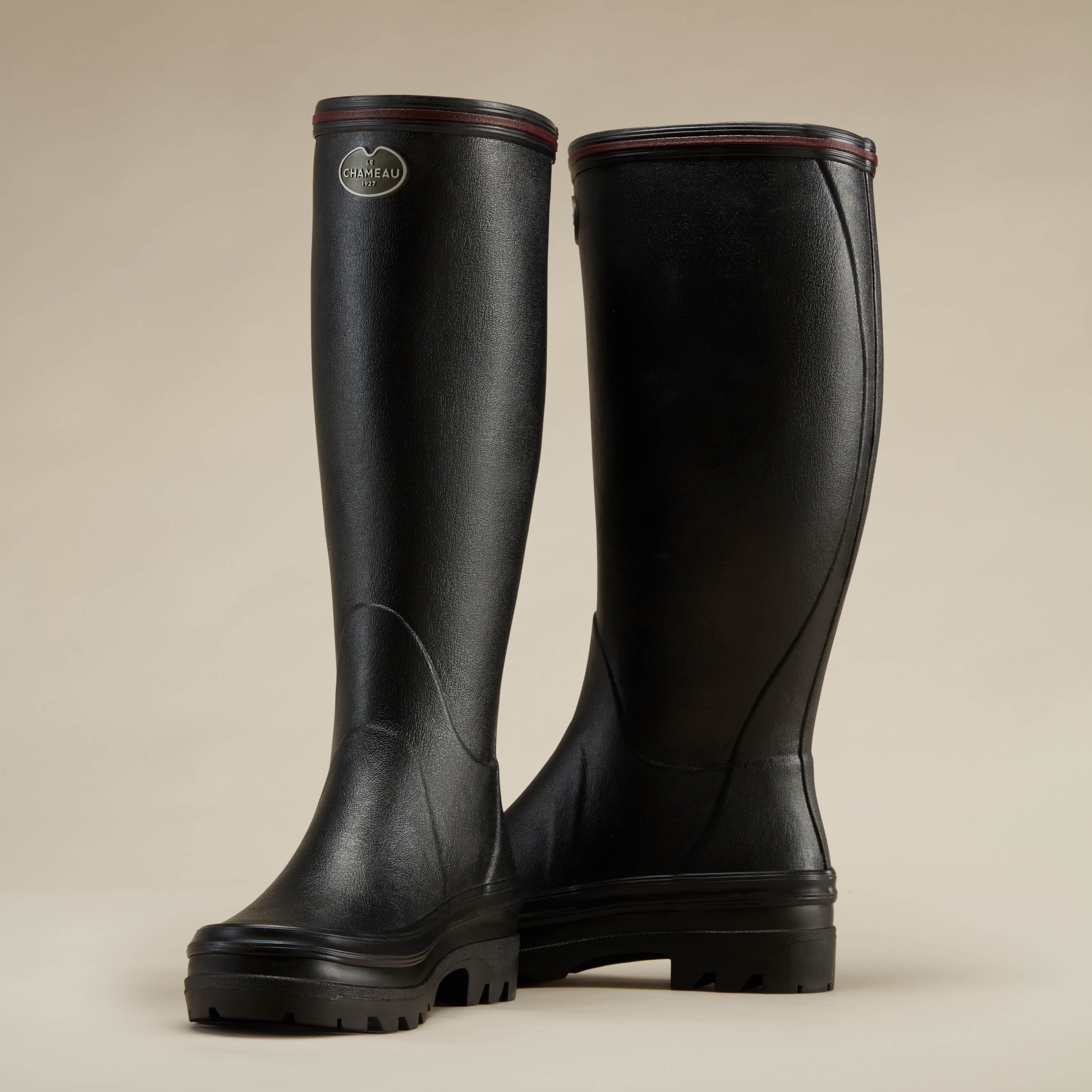 Reverse three-quarter view of a pair of Women's Giverny Jersey Lined Wellington Boot in Black on a beige background. The outer boot shows the logo badge and front profile, while the inner boot highlights the boot’s curved seam detailing and back shaft contour.