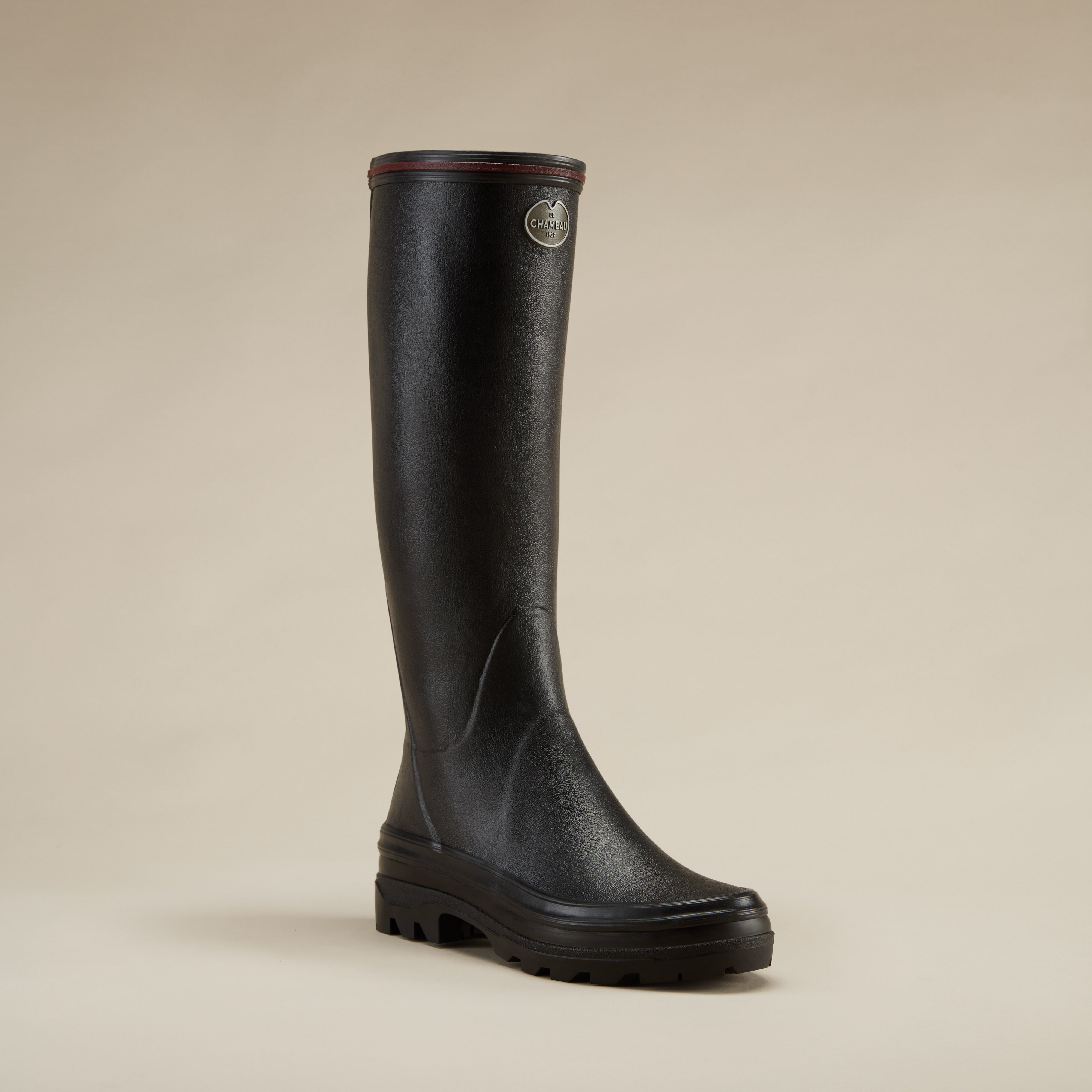 Front-side angled view of a single Women's Giverny Jersey Lined Wellington Boot in Black with a burgundy trim and visible logo badge on the outer side. The boot stands against a neutral background, highlighting its ergonomic shape and high-traction sole.