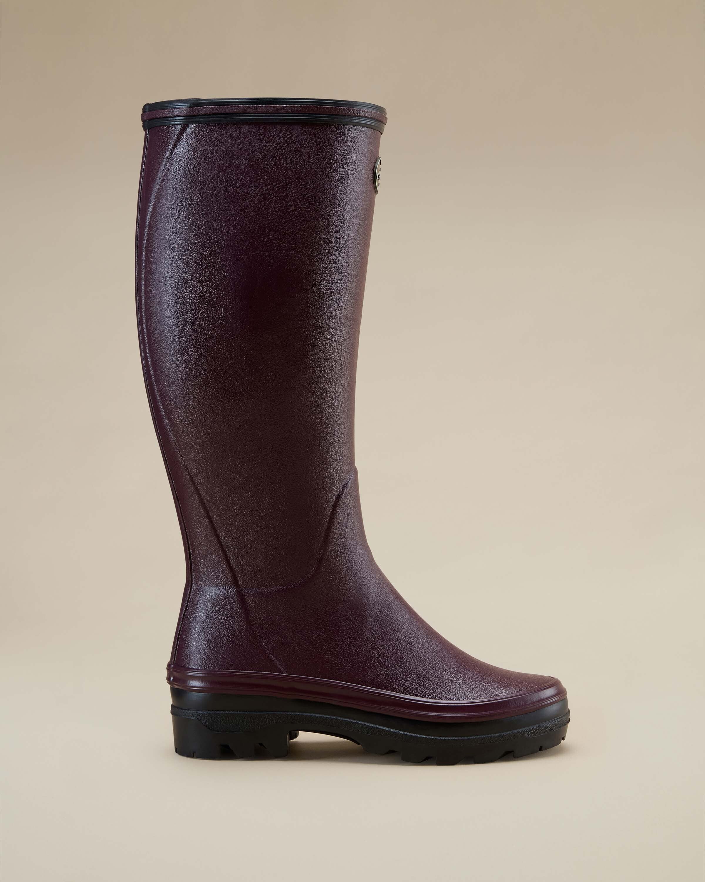 Profile view of the Women's Giverny Jersey Lined Wellington Boot in Cherry Red standing alone on a beige background. The boot’s minimalistic design, high shaft, and black treaded sole are clearly visible, with a smooth, matte finish.