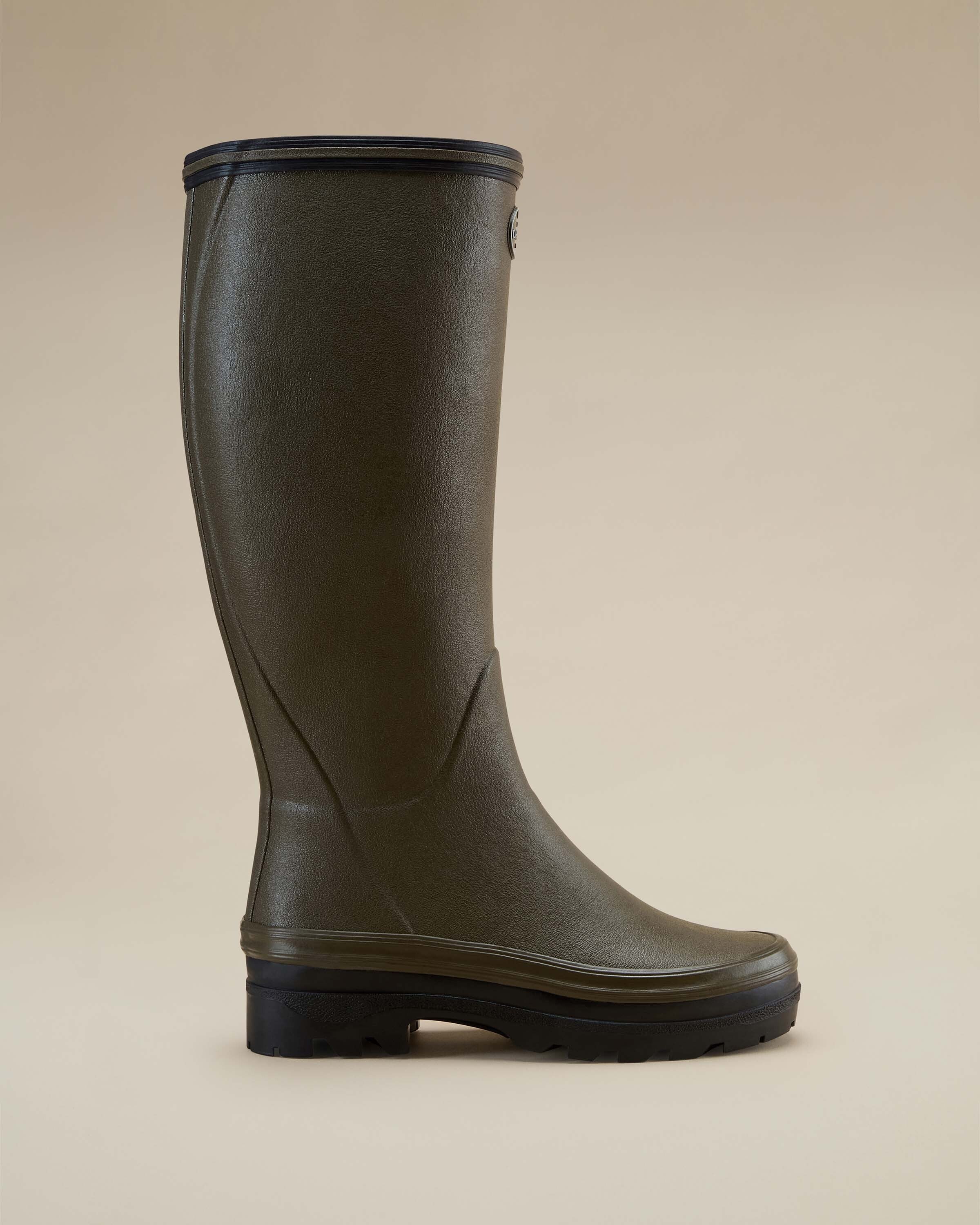 Full side profile of a Women's Giverny Jersey Lined Wellington Boot in Chameau Green with black outsole and trim, displayed on a clean beige background to highlight its minimalist elegance.