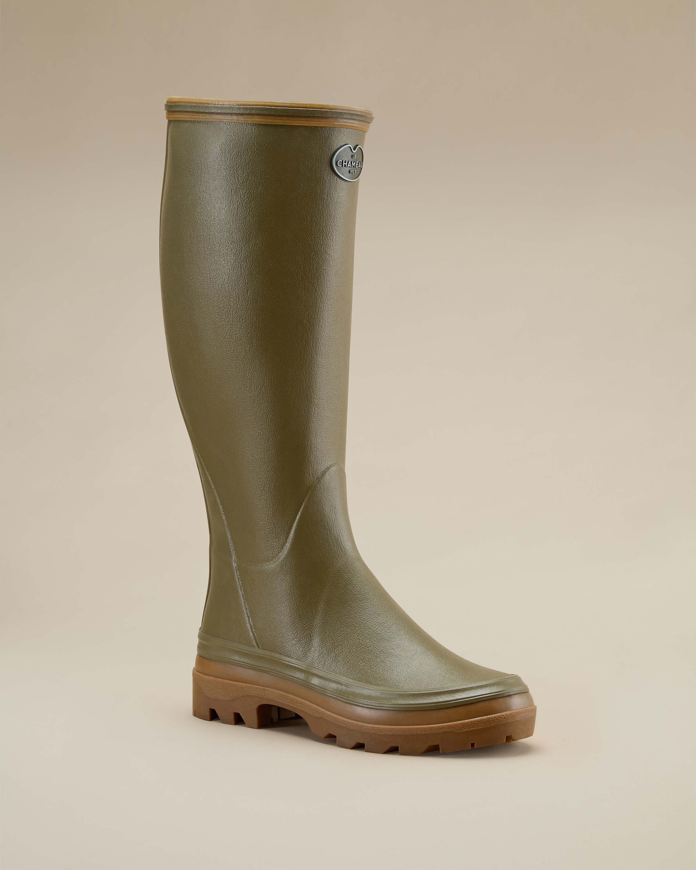 A single Women's Giverny Jersey Lined Wellington Boot in Iconic Green is displayed at a front three-quarter angle against a beige background. The boot's elegant curve, structured ankle, and reinforced toe box are visible. The brown lug sole adds depth and contrast.