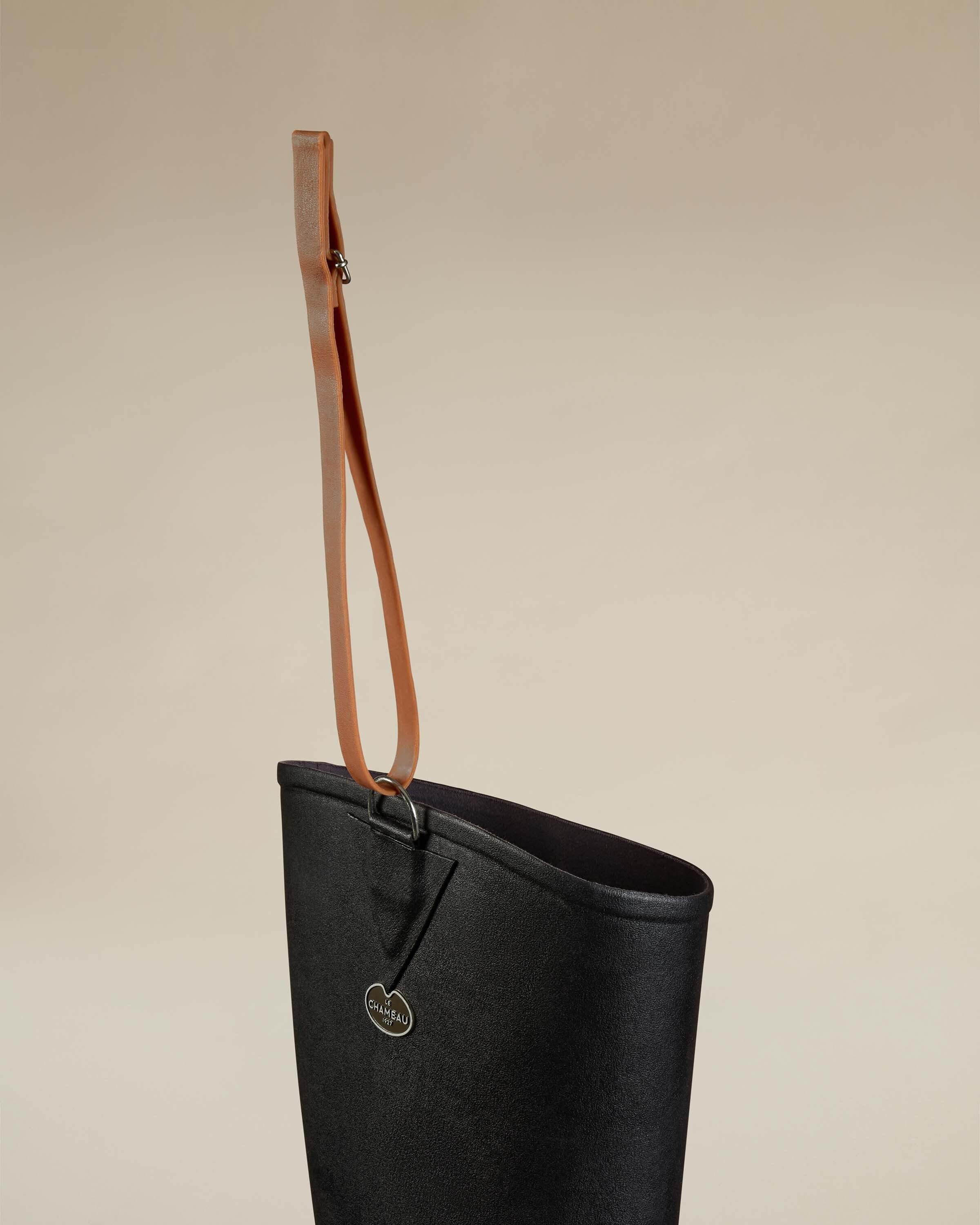 Close-up of the upper portion of the Women's Océane Ponti Lined Thigh Boot in Black, focusing on the brown leather hanging strap and metallic attachment ring stitched into a reinforced patch near the top edge.