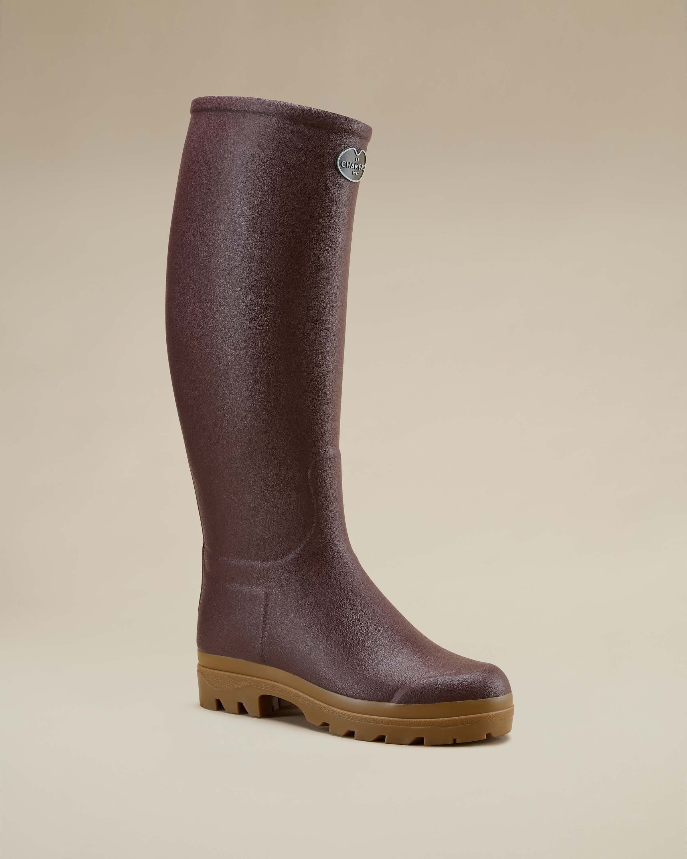 A single Women's Saint Hubert Leather Lined Wellington Boot in Brown displayed at a three-quarter angle, showing the boot’s rounded toe, upper curvature, and outsole treading. The logo badge is visible near the top of the shaft, and the light reflects subtly off the textured rubber.