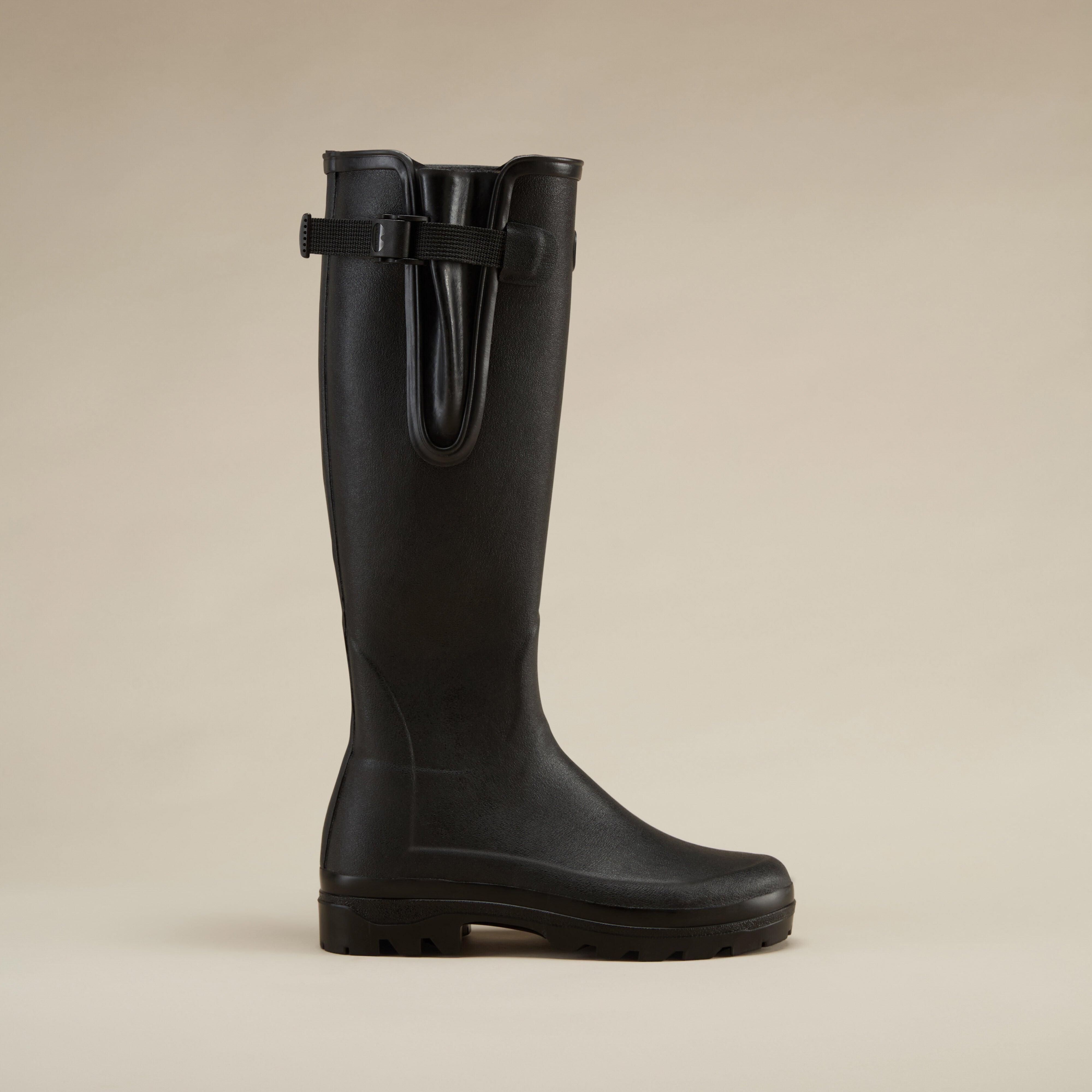 Straight side profile of a single Women's Vierzonord Neoprene Lined Wellington Boot in Black on a beige background, emphasizing the sleek rubber construction and structured fit.