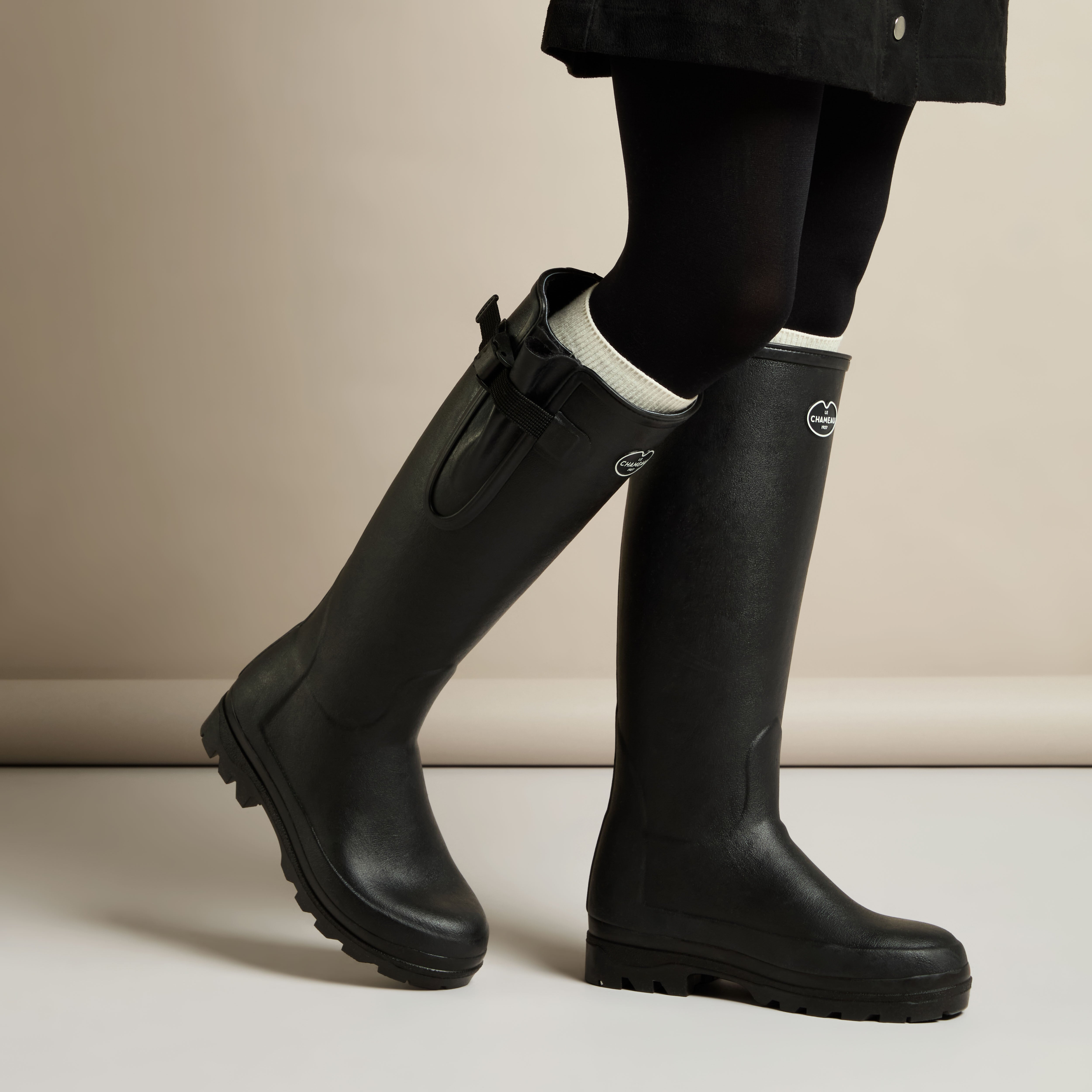 Model walking in a pair of Women's Vierzonord Neoprene Lined Wellington Boot in Black styled with a black skirt and white socks, showcasing the boots’ fit and movement in a lifestyle setting.
