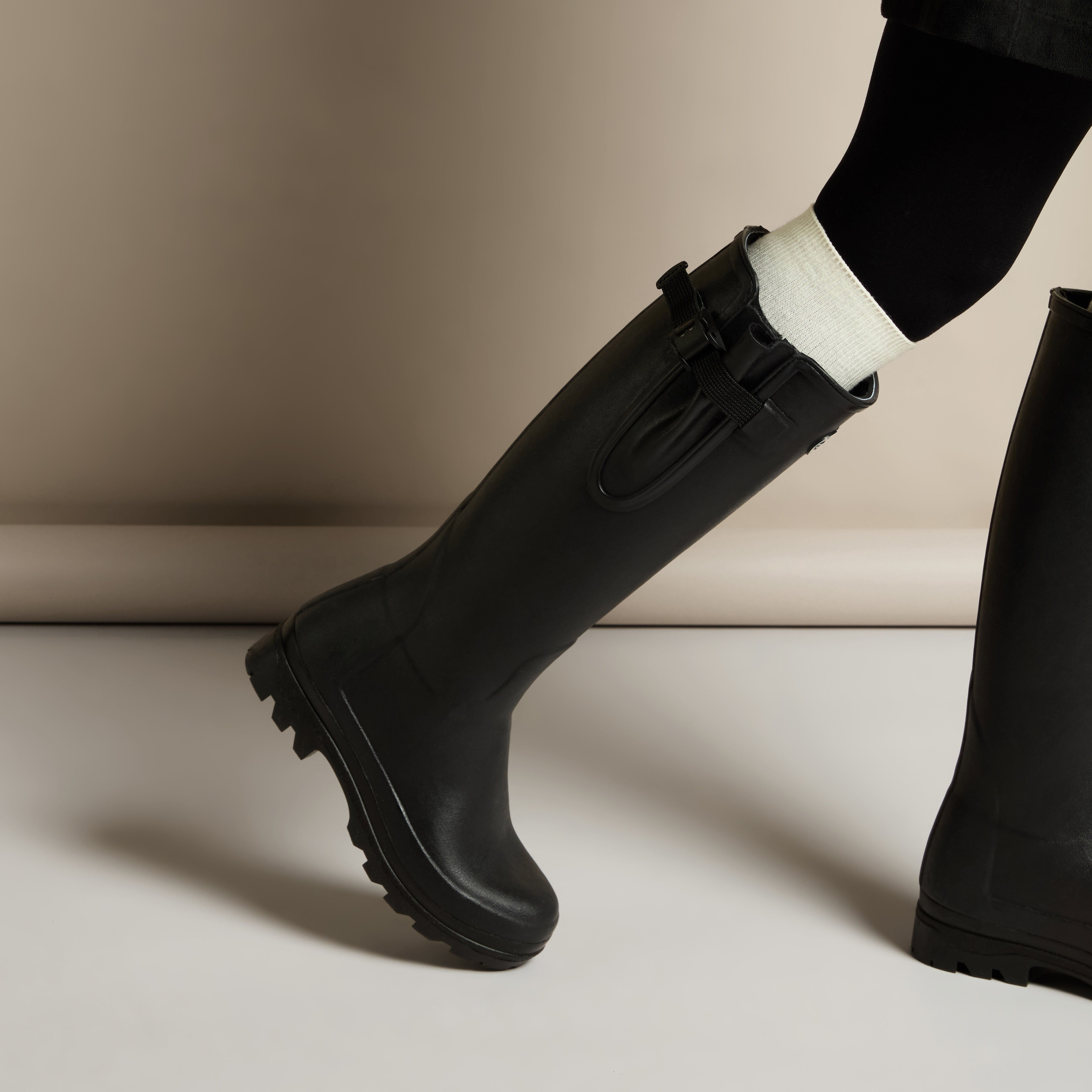 Lifestyle shot of a model wearing Women's Vierzonord Neoprene Lined Wellington Boot in Black with one leg extended forward, emphasizing the boot’s elegant silhouette and outdoor-ready construction.