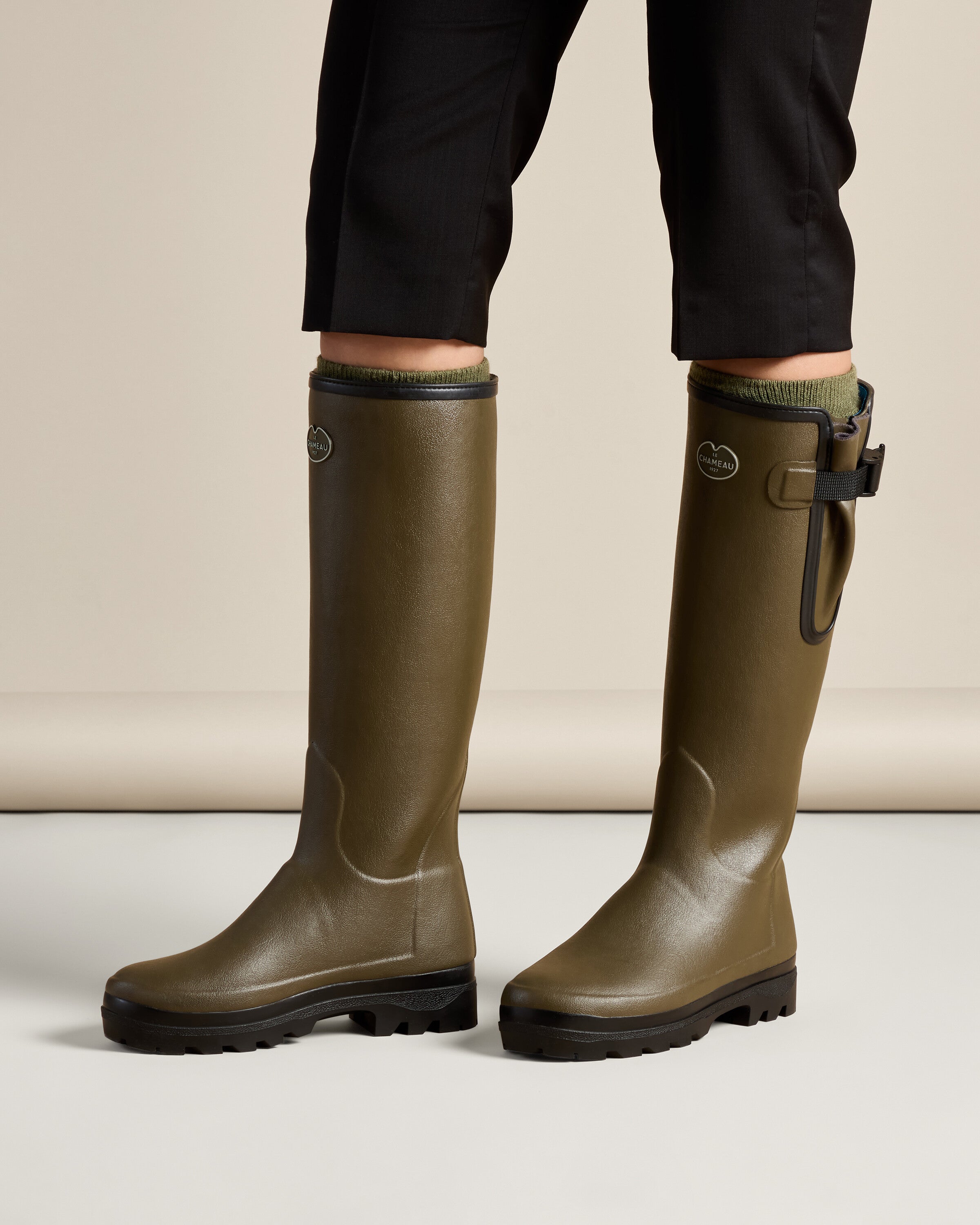 Another on-model image from the front side angle, showing the Women's Vierzonord Neoprene Lined Wellington Boot in Chameau Green mid-step. The gusset and black strap are visible, emphasizing adjustability and mobility in the design.