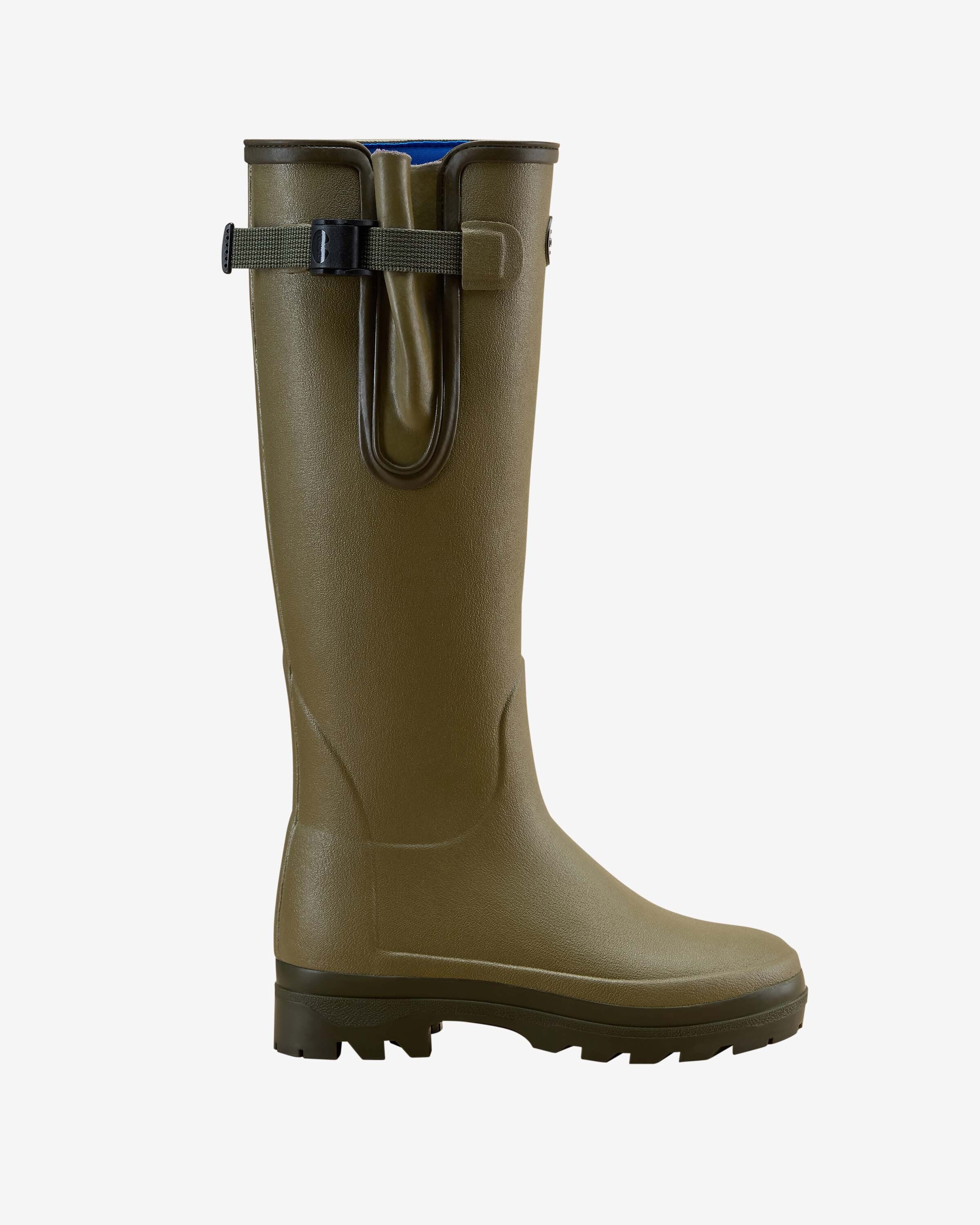 A pair of Women's Vierzonord Neoprene Lined Wellington Boot in Iconic Green colorway worn by a model. The boots feature a slightly matte olive-toned rubber exterior, a distinctive tightening strap with a snap-fastening buckle, and Le Chameau's signature oval logo badge on the outer shaft. The model wears the boots with off-white trousers tucked in, highlighting the tall shaft and rugged tread.