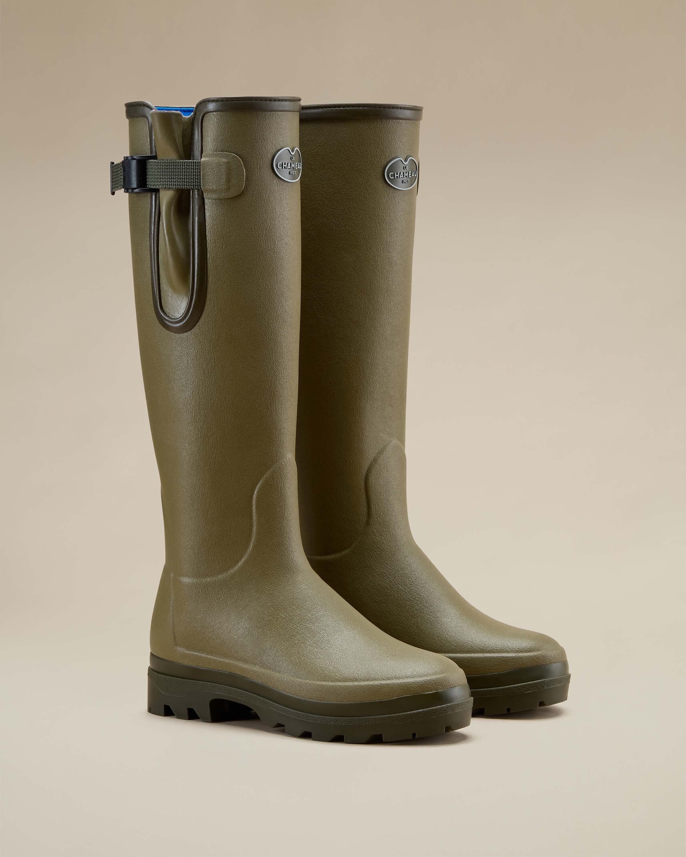 A single Women's Vierzonord Neoprene Lined Wellington Boot in Iconic Green colorway, presented against a clean white background in a side profile view. The image emphasises the textured rubber surface, contoured panels, and the adjustable gusset strap with a green webbing and plastic buckle, along with the brand's logo plaque and the visible blue neoprene lining.