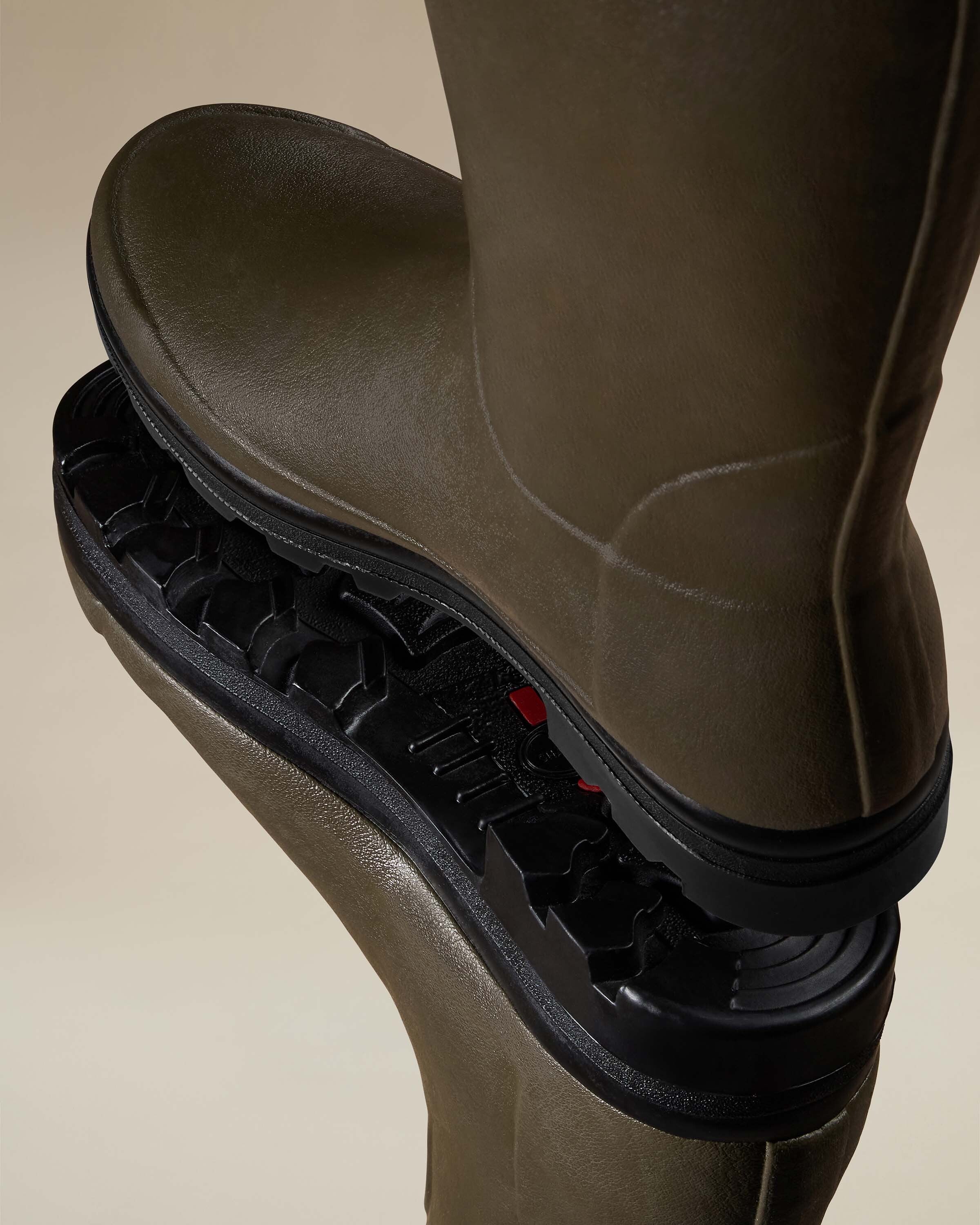 Artistic macro shot of the Men's Vierzonord Neoprene Lined Wellington Boot in Chameau Green soles stacked against each other, emphasizing the aggressive lug tread design and durable black rubber outsole. The red rubber inserts add contrast, showcasing the grip and terrain traction features of the Le Chameau men's Vierzonord boot.