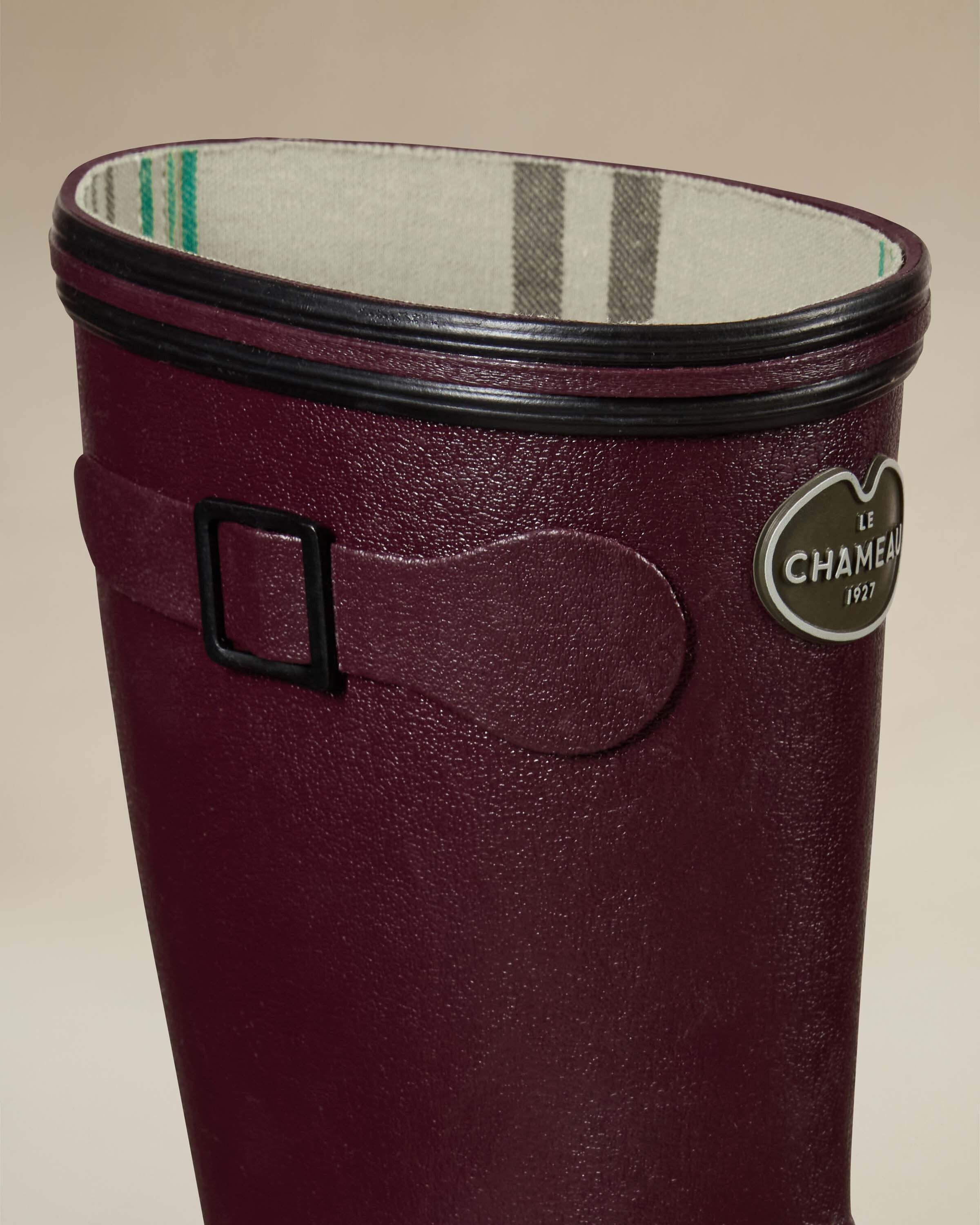 Close-up of the upper section of the Women's Giverny Jersey Lined Bottillon in Cherry Red. Focused on the logo badge, buckle strap, and interior lining, the image reveals the jersey lining’s plaid pattern in green, grey, and cream tones.