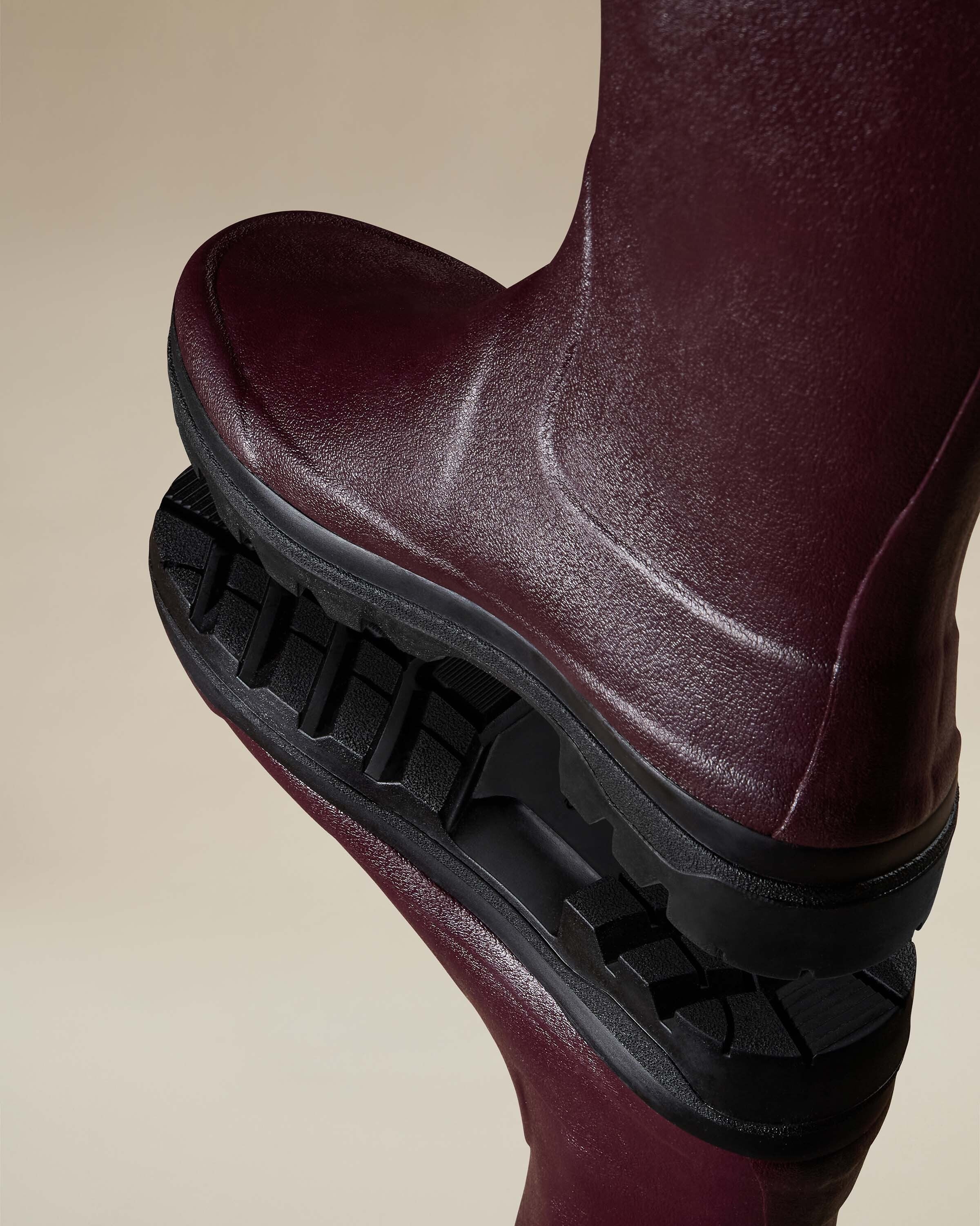 Macro shot showing one Women's Giverny Jersey Lined Bottillon in Cherry Red stacked on another. The image emphasises the sole’s deep tread pattern and showcases the high-quality texture of the rubber construction.