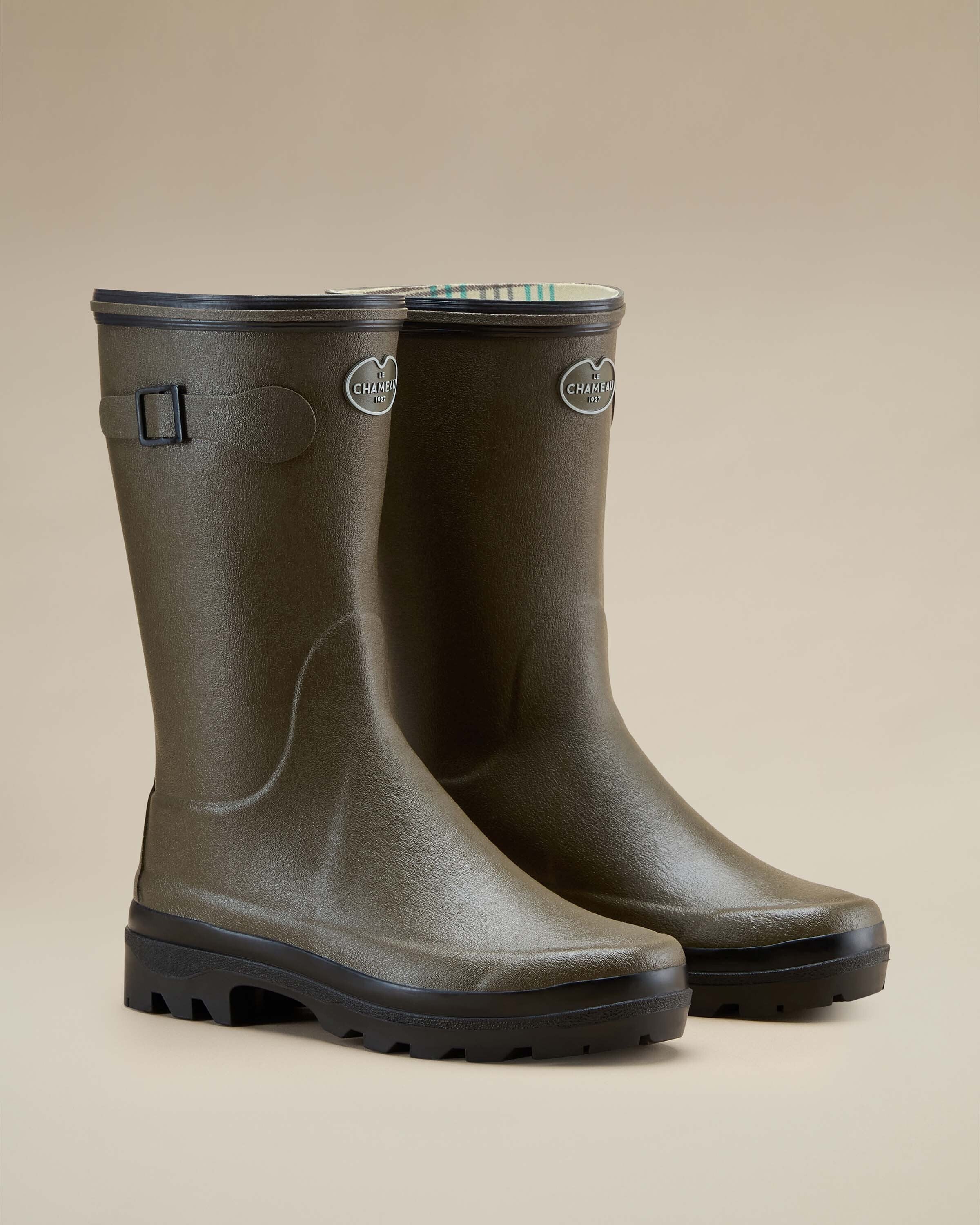 Three-quarter angled view of a pair of Women's Giverny Jersey Lined Bottillon in Chameau Green. The boots stand upright with visible brand logos and decorative side buckles. The interior lining with a striped pattern is slightly visible.