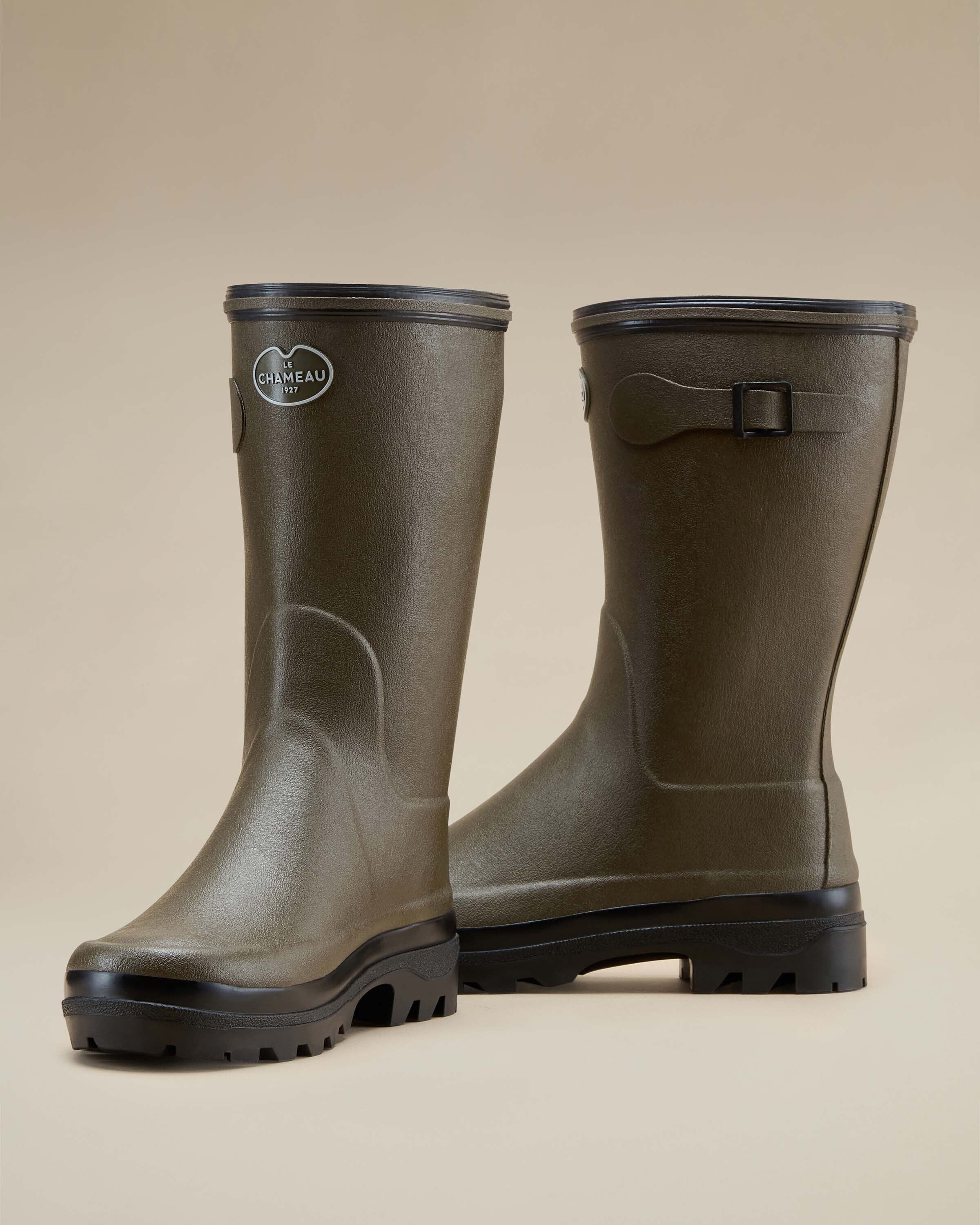 Front-side angled view of a pair of Women's Giverny Jersey Lined Bottillon in Chameau Green. Set against a neutral tan backdrop, the boots display both the front and side profile, including the logo badge and buckle detail.