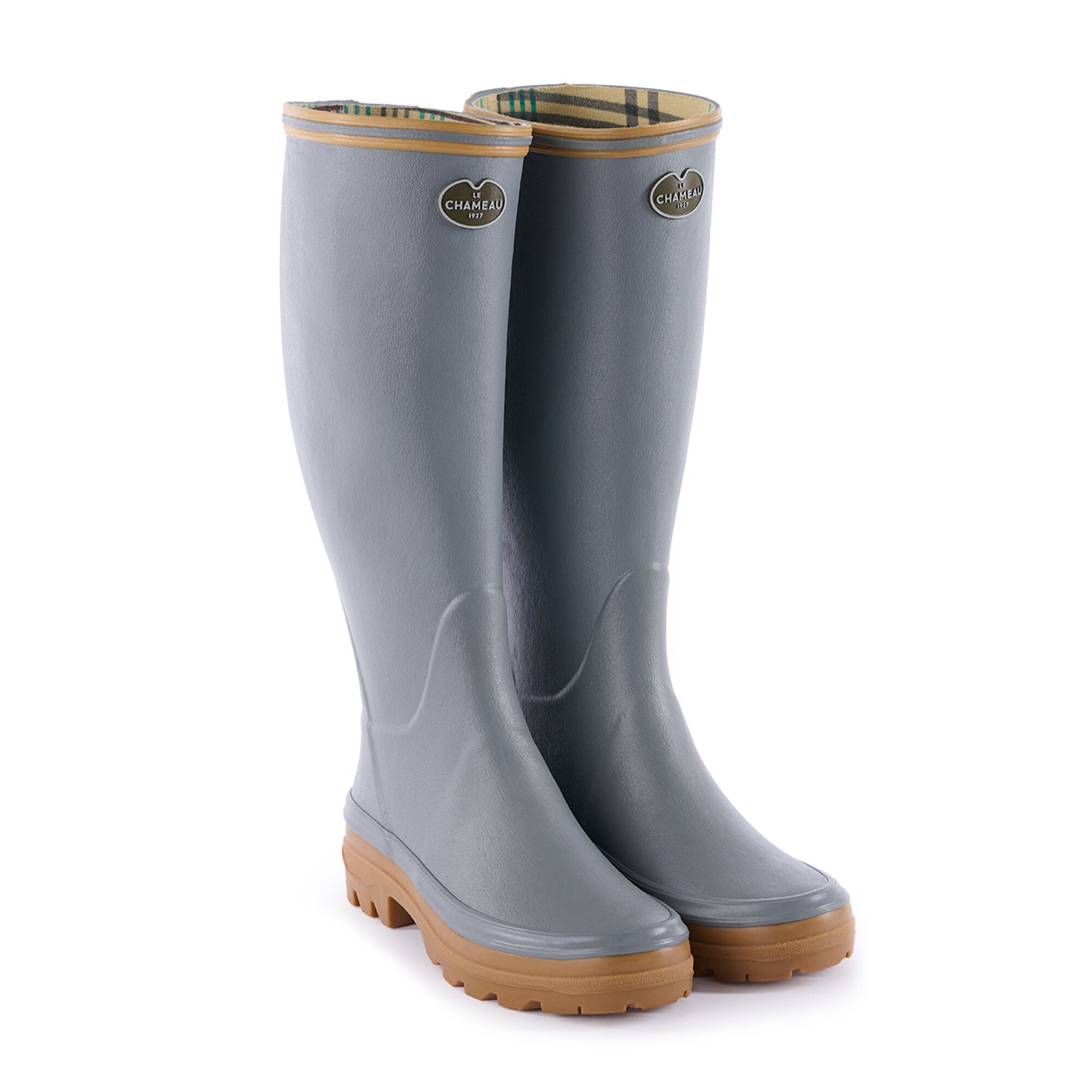 A pair of Women's Giverny Jersey Lined Wellington Boot in Grey standing upright on a white background. The boots are light gray with tan soles and tan trim at the opening. The interiors are lined with a patterned fabric featuring green and brown stripes. Each boot features a silver-tone Le Chameau logo badge on the front-facing upper shaft.