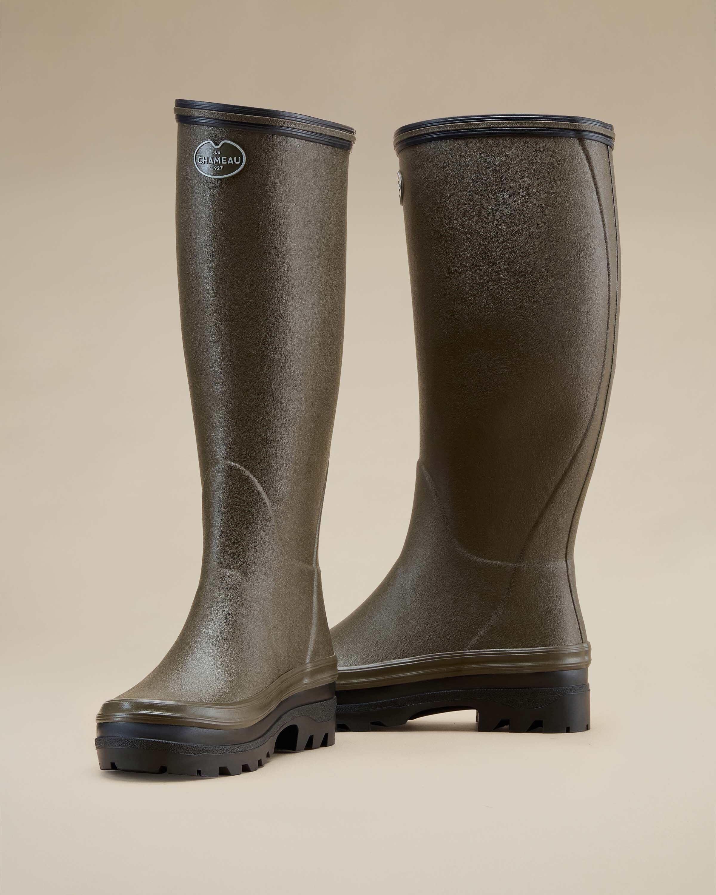 A silhouetted angled view of the Women's Giverny Jersey Lined Wellington Boot in Chameau Green, accentuating the structured upper, reinforced heel, and premium handcrafted rubber texture on a neutral beige backdrop.
