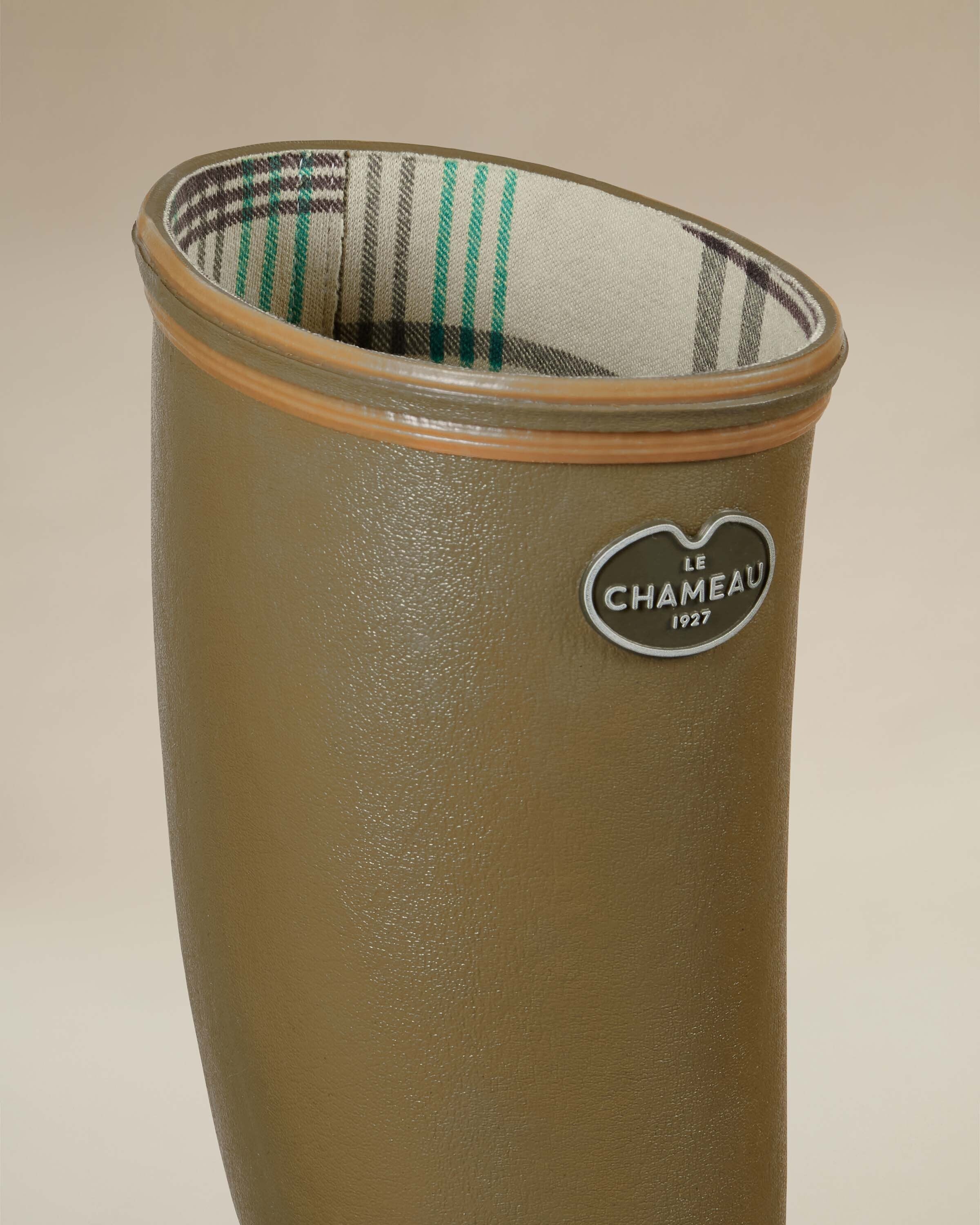 A close-up of the top of the Women's Giverny Jersey Lined Wellington Boot in Iconic Green focuses on the inner plaid jersey lining with green and black stripes. The textured rubber exterior and brown top trim are also clearly visible. The Le Chameau metallic logo badge is prominently displayed.