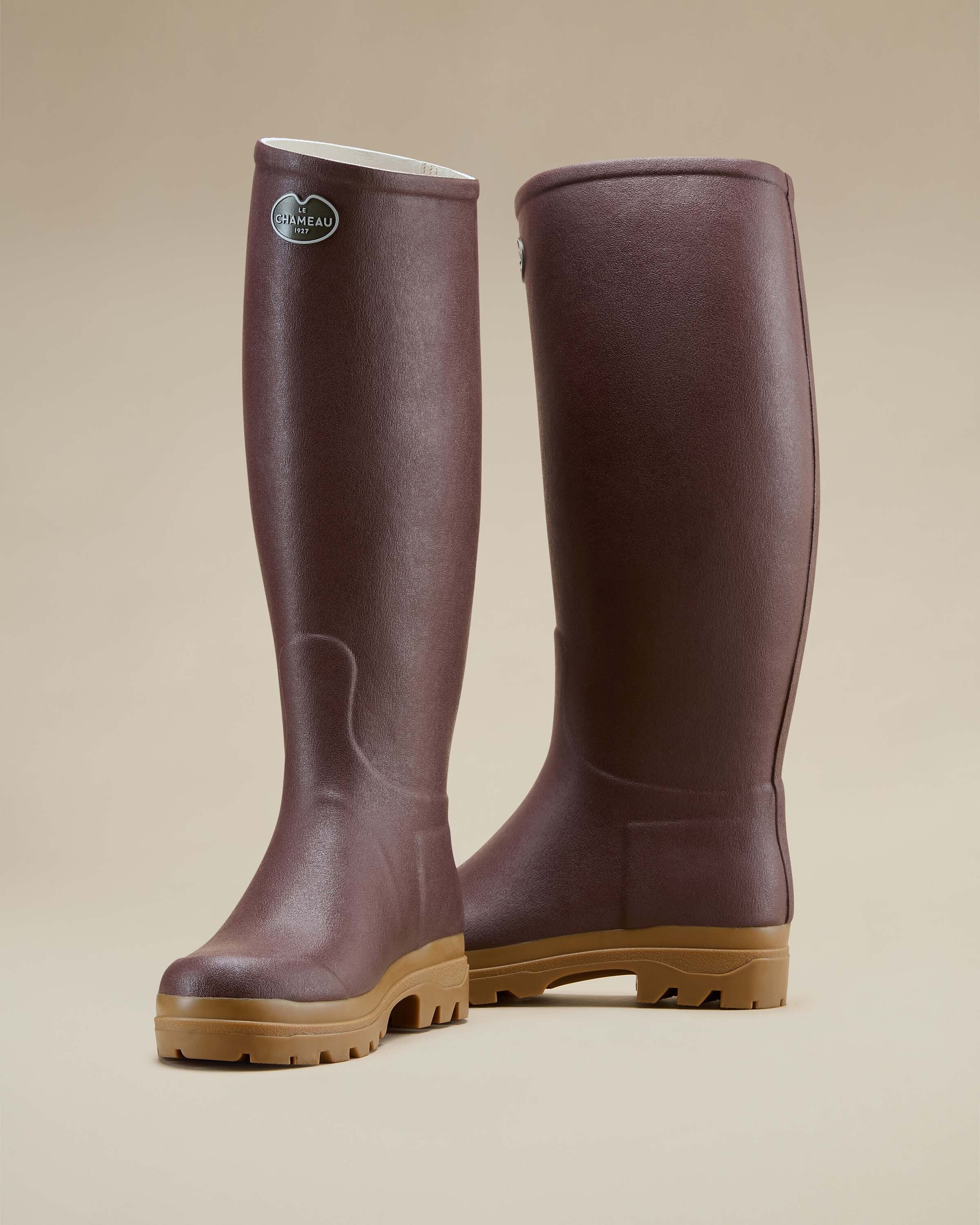 A rear angle view of a pair of Women's Saint Hubert Leather Lined Wellington Boot in Brown placed on a beige surface, showing both the side and back details. The photo emphasises the shape and structure of the boot shafts and how they taper slightly near the calves.