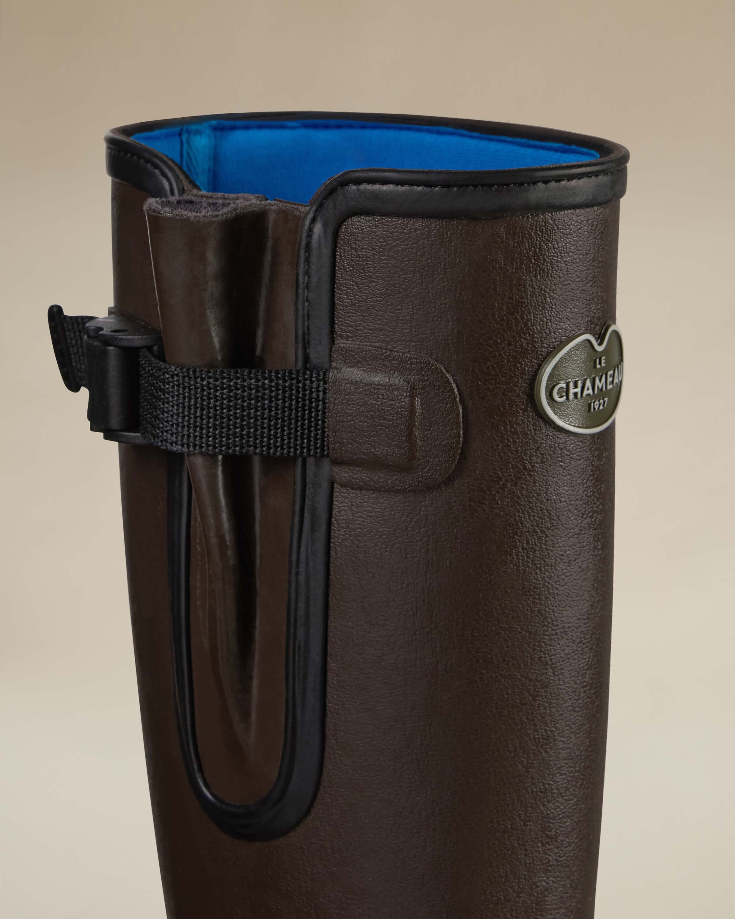 Close-up detail shot of the upper shaft of the Women's Vierzonord Neoprene Lined Wellington Boot in Dark Brown, revealing the inside blue neoprene lining for thermal insulation, the structured waterproof gusset with molded side panels, and the branded black adjustable strap. The texture of the rubber and the craftsmanship of the reinforced collar lining are clearly visible, demonstrating comfort and durability.