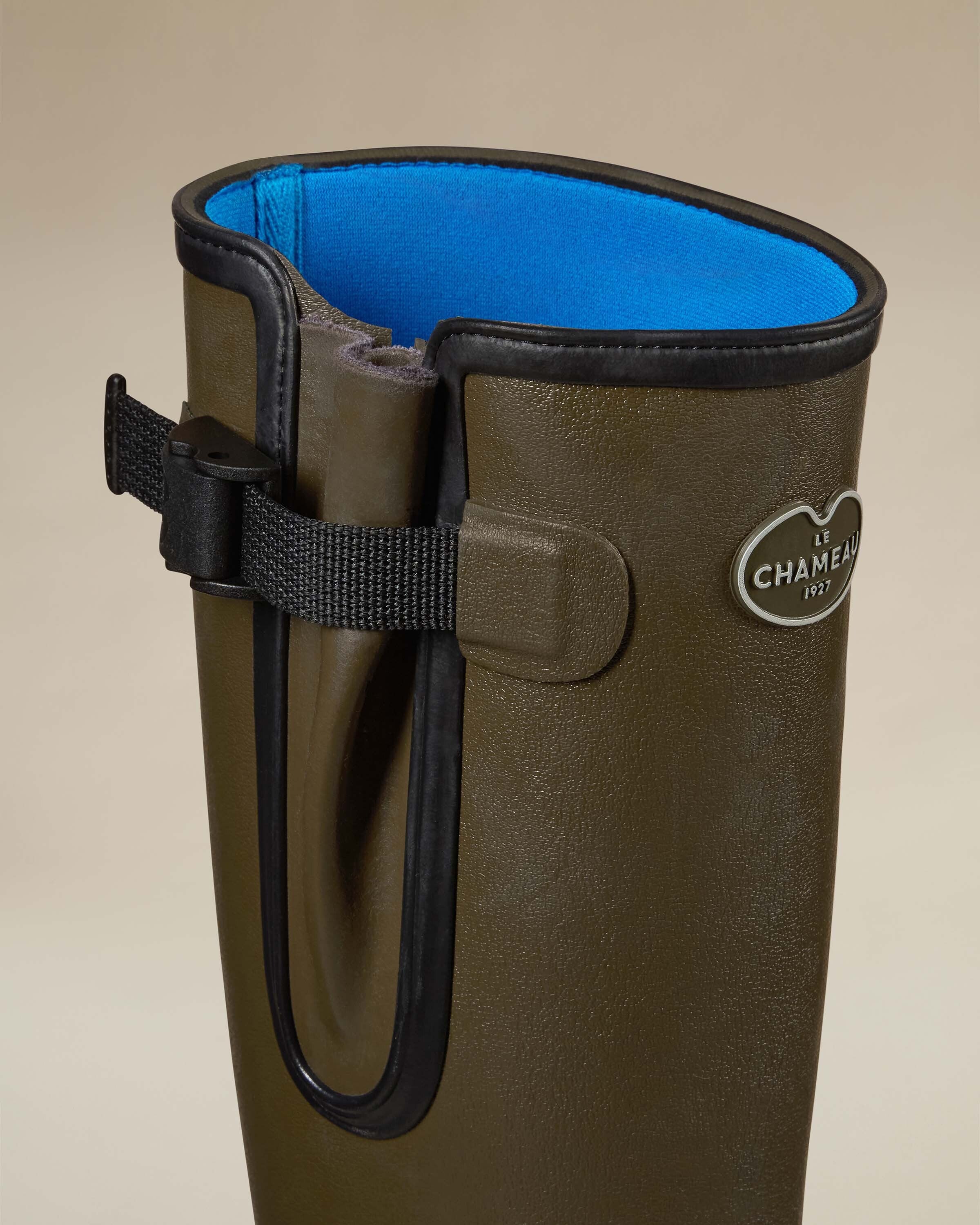 Close-up of the Women's Vierzonord Neoprene Lined Wellington Boot in Chameau Green’s top section, highlighting the textured olive green exterior, bold black trim, gusset strap with buckle closure, and the vivid blue neoprene inner lining. The Le Chameau 1927 logo badge is also clearly visible.